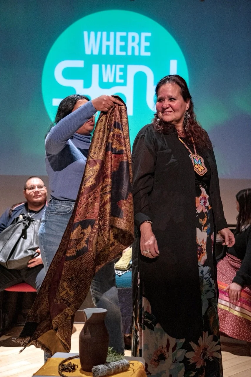 A person is putting a scarf on an other person with a Where We Stand logo in the background.