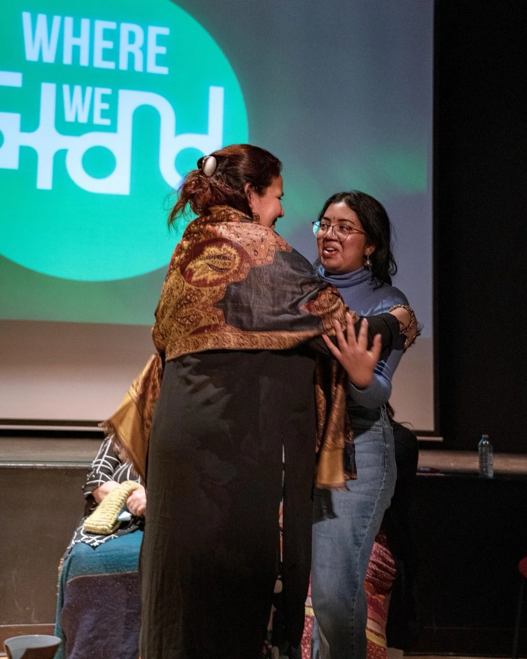 Two people hugging front of the Where We Stand in logo.
