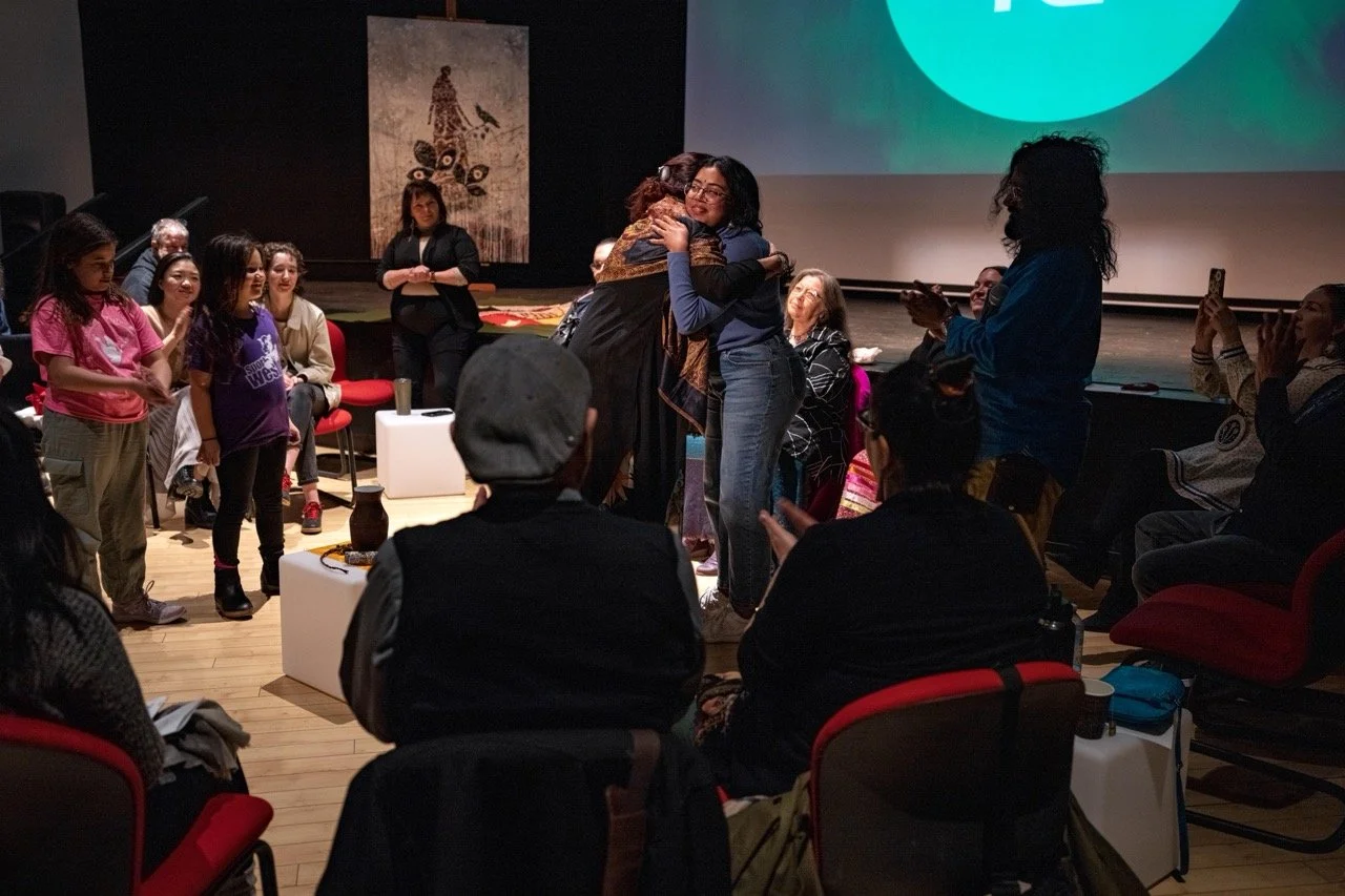 Wide angle of two person hugging front of an audience.