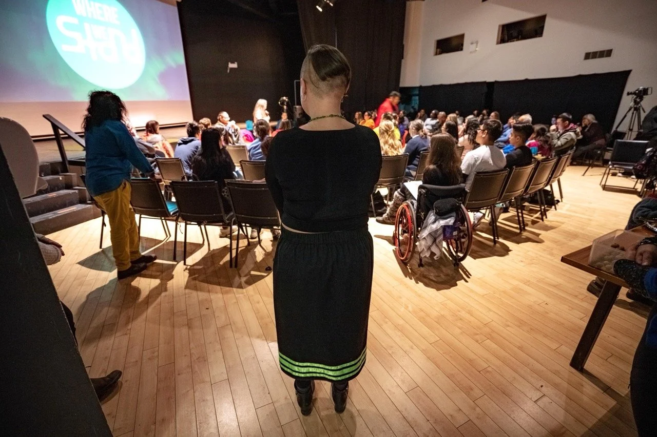 Wide angle of a room full of people watching a presentation with a person in standing behind them.