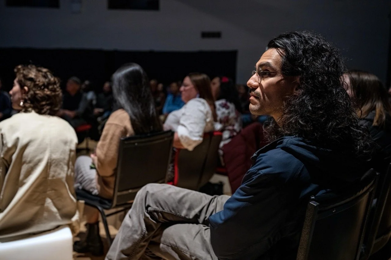 Close up of person wearing a blue shirt in the audience watching a performance.
