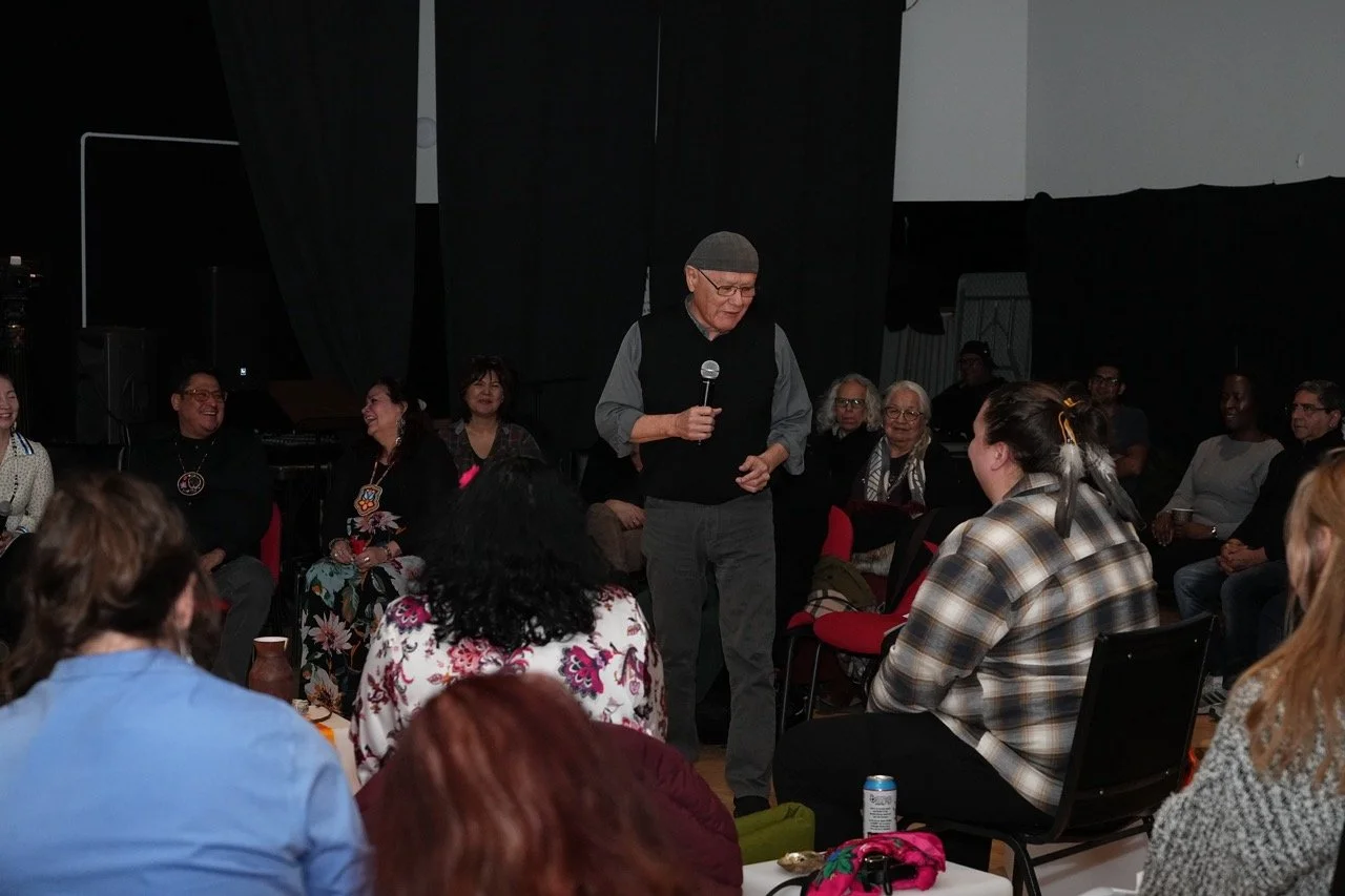 Person with hat on is holding a microphone in the middle of a circle front of an audience.