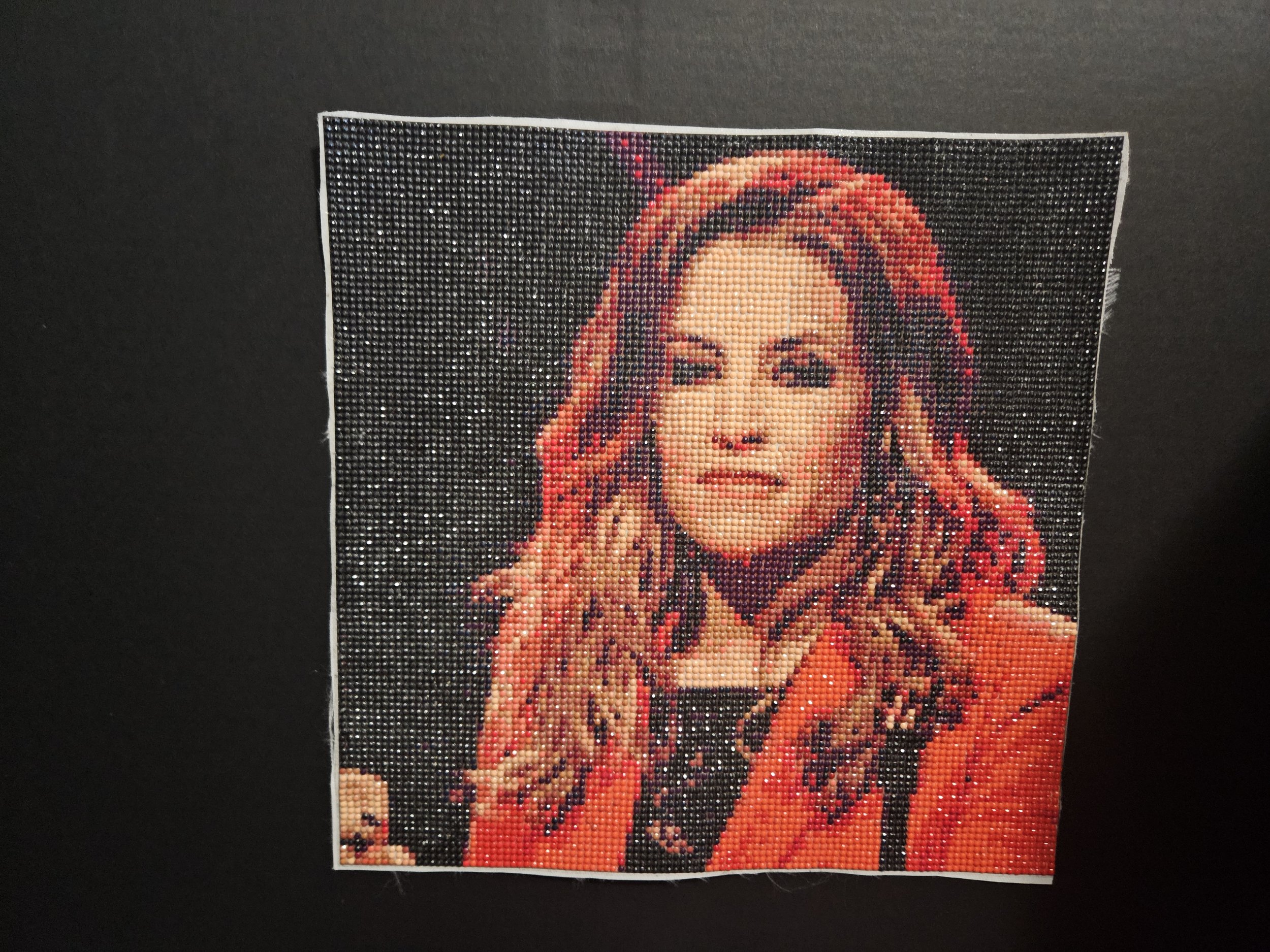 A pixelated artwork of Lisa Marie Presley with long hair in a red outfit on a dark background.