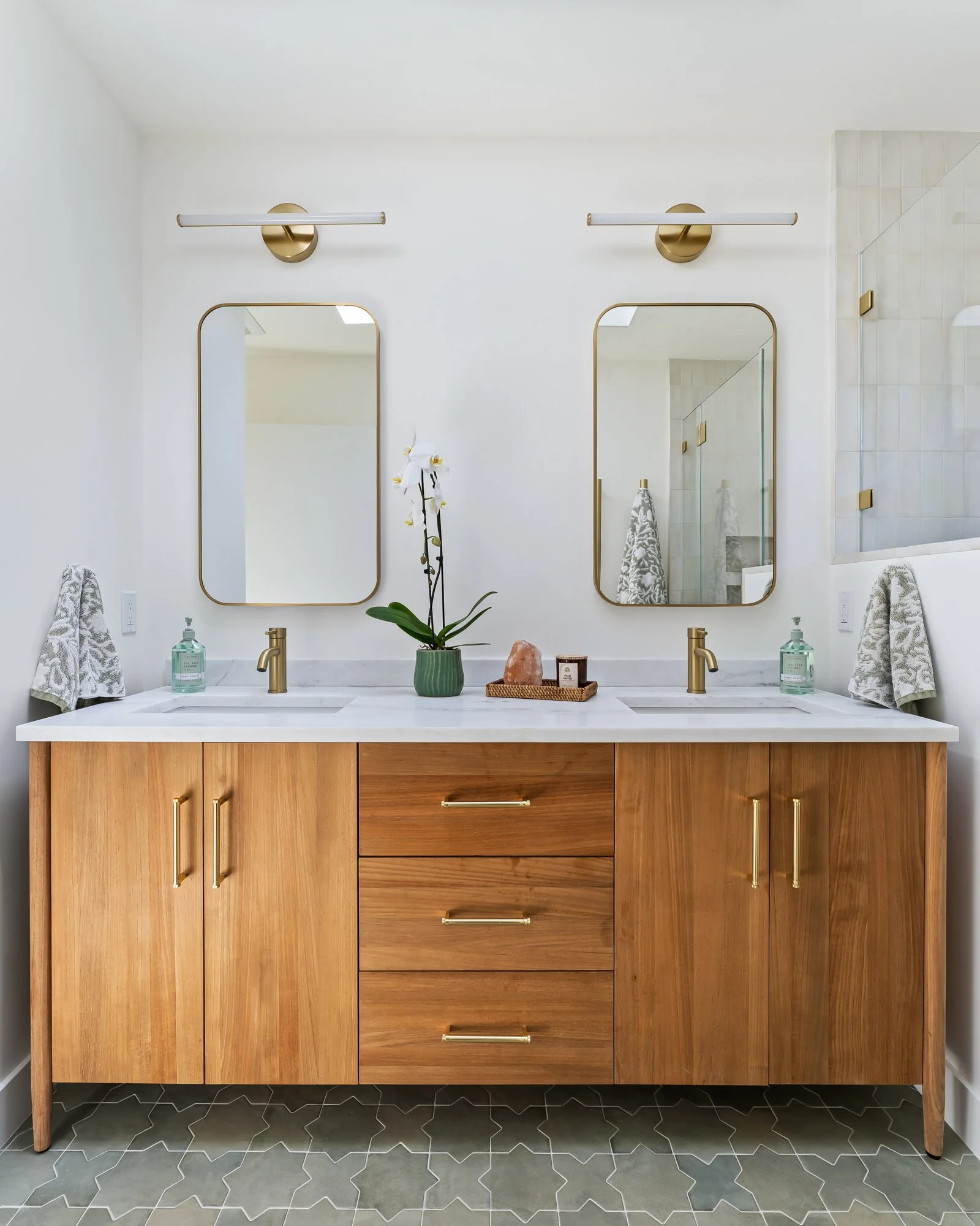 Modern double vanity with warm walnut cabinetry, a white quartz countertop, brushed brass fixtures, and arched mirrors in a custom Santa Cruz bathroom remodel.