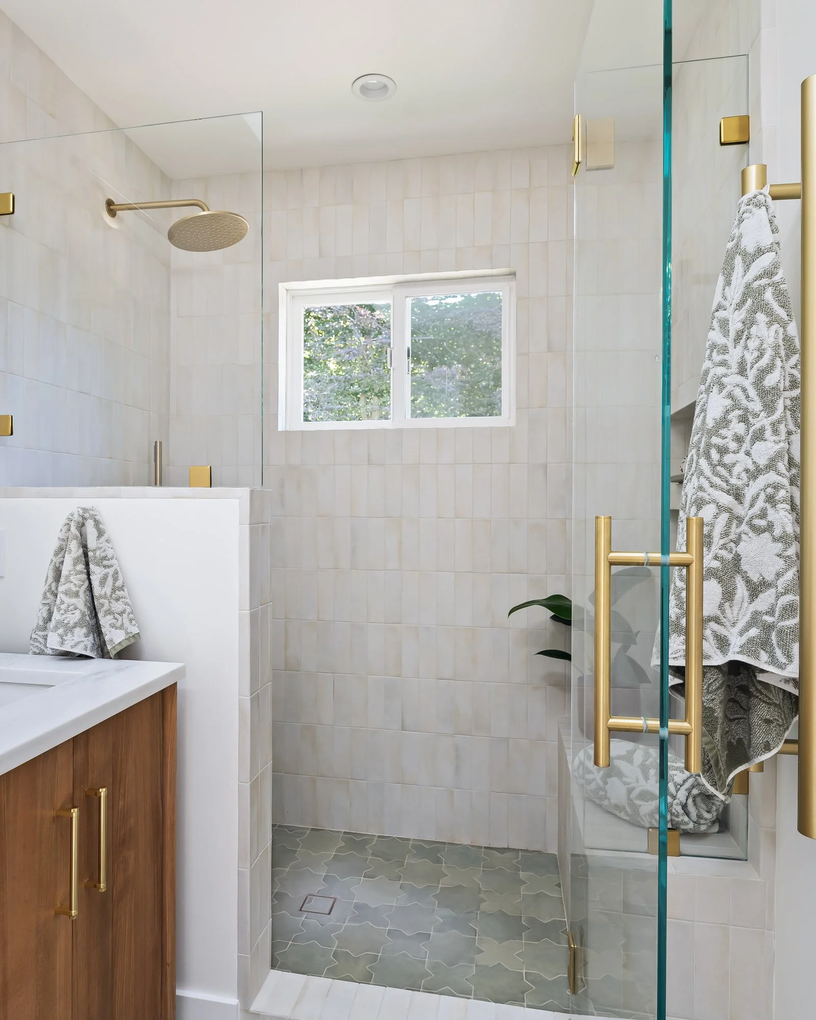 Bright walk-in shower featuring porcelain tile, frameless glass, and brushed brass hardware.