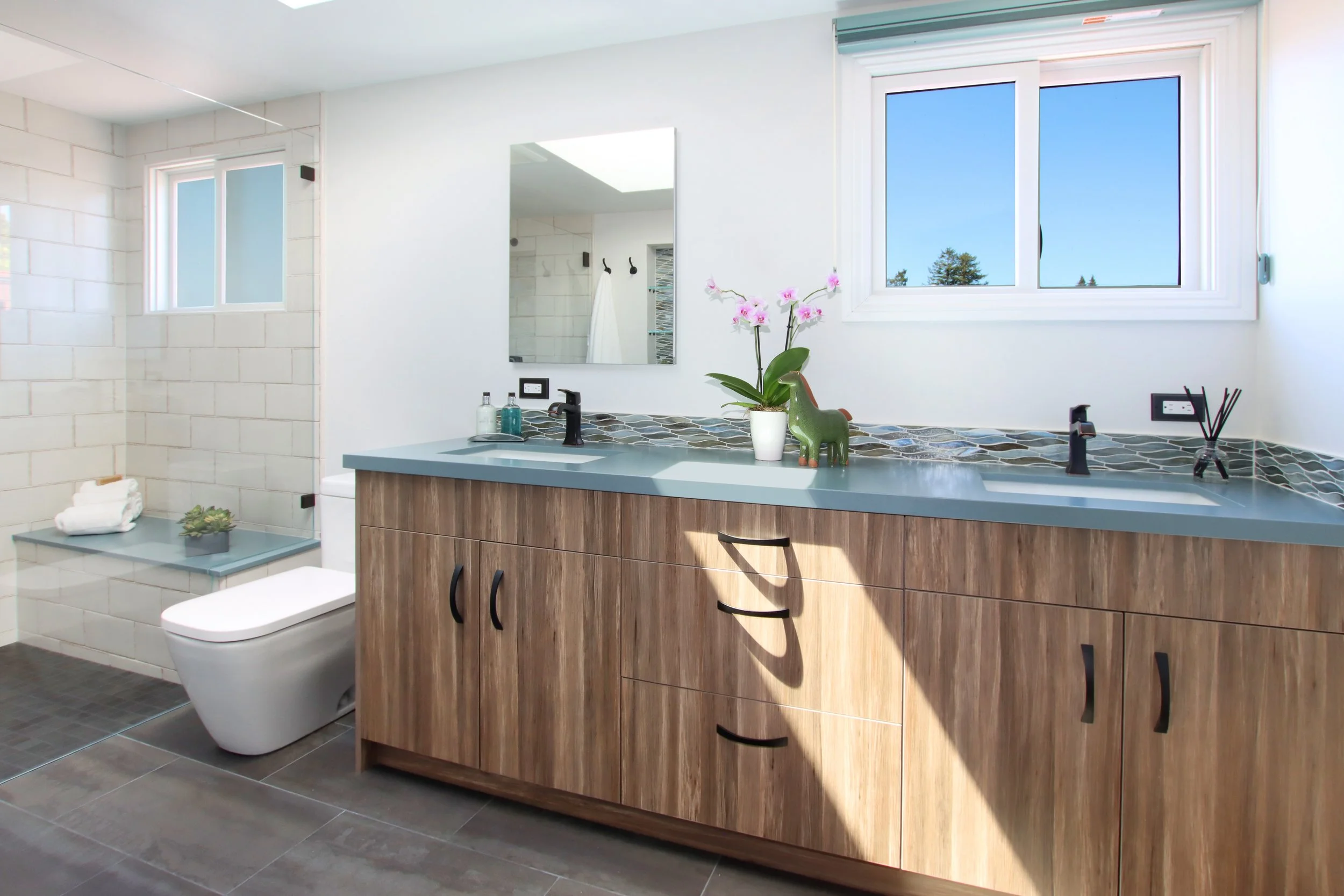 Bathroom remodel in Santa Cruz County with double walnut vanity, blue-gray stone countertop, matte black fixtures, and walk-in shower