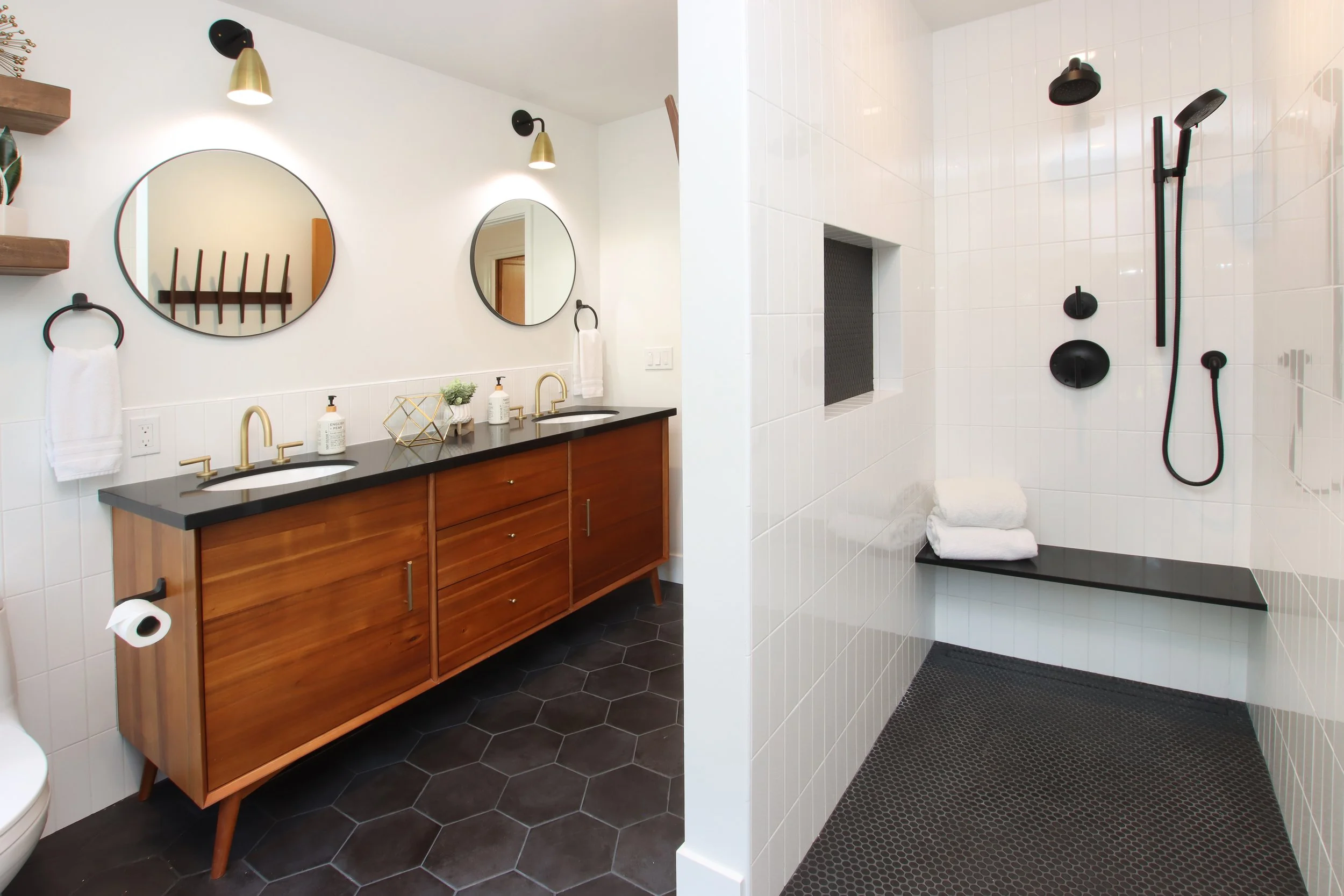 Custom bathroom renovation featuring a wood double vanity, round mirrors, brass fixtures, and a walk-in shower with bench in a Santa Cruz County home.