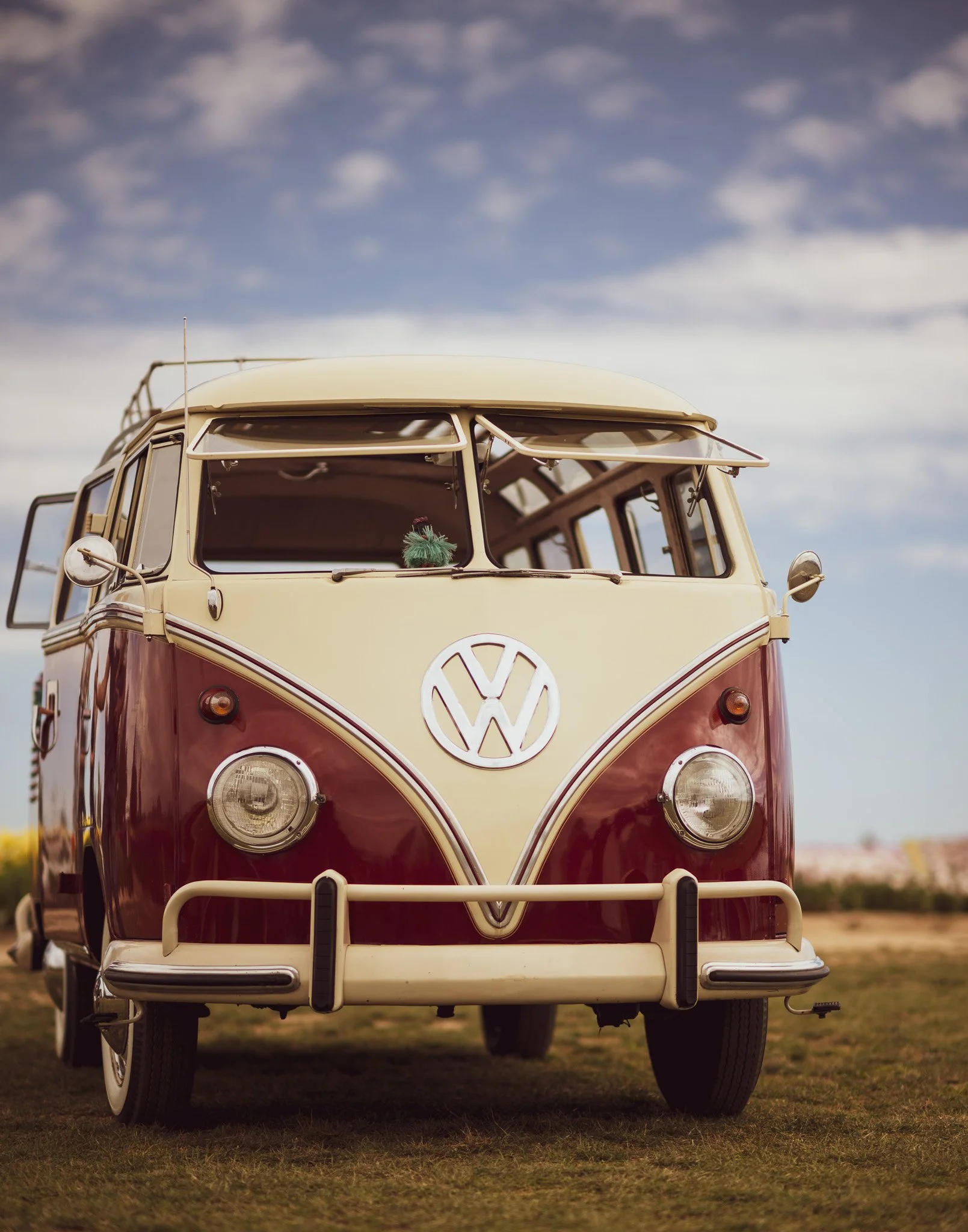 Vintage Volkswagen Type 2 van with cream and red paint parked on grass under a cloudy sky.