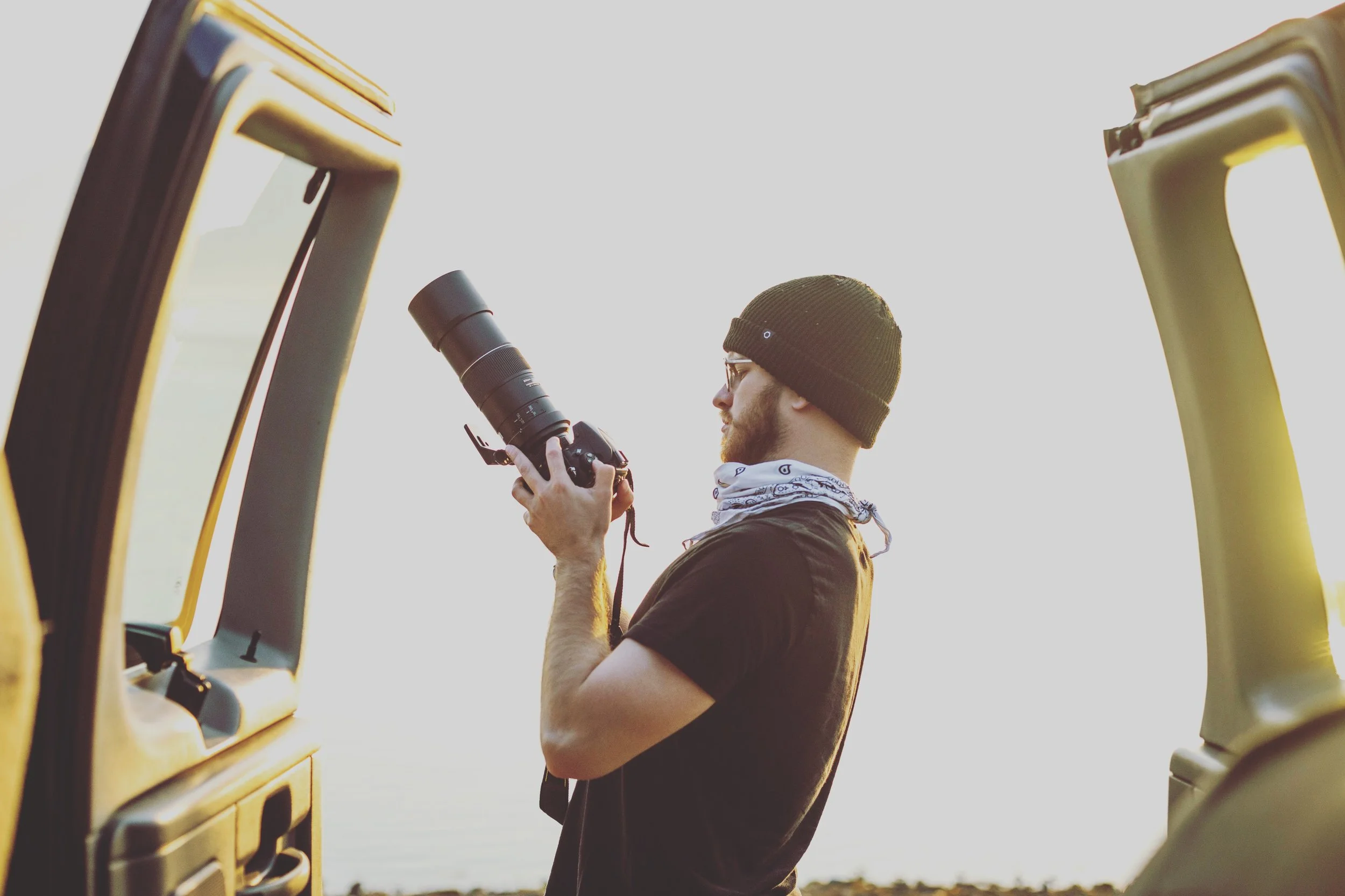 Man with beanie holding a DSLR camera near open car doors
