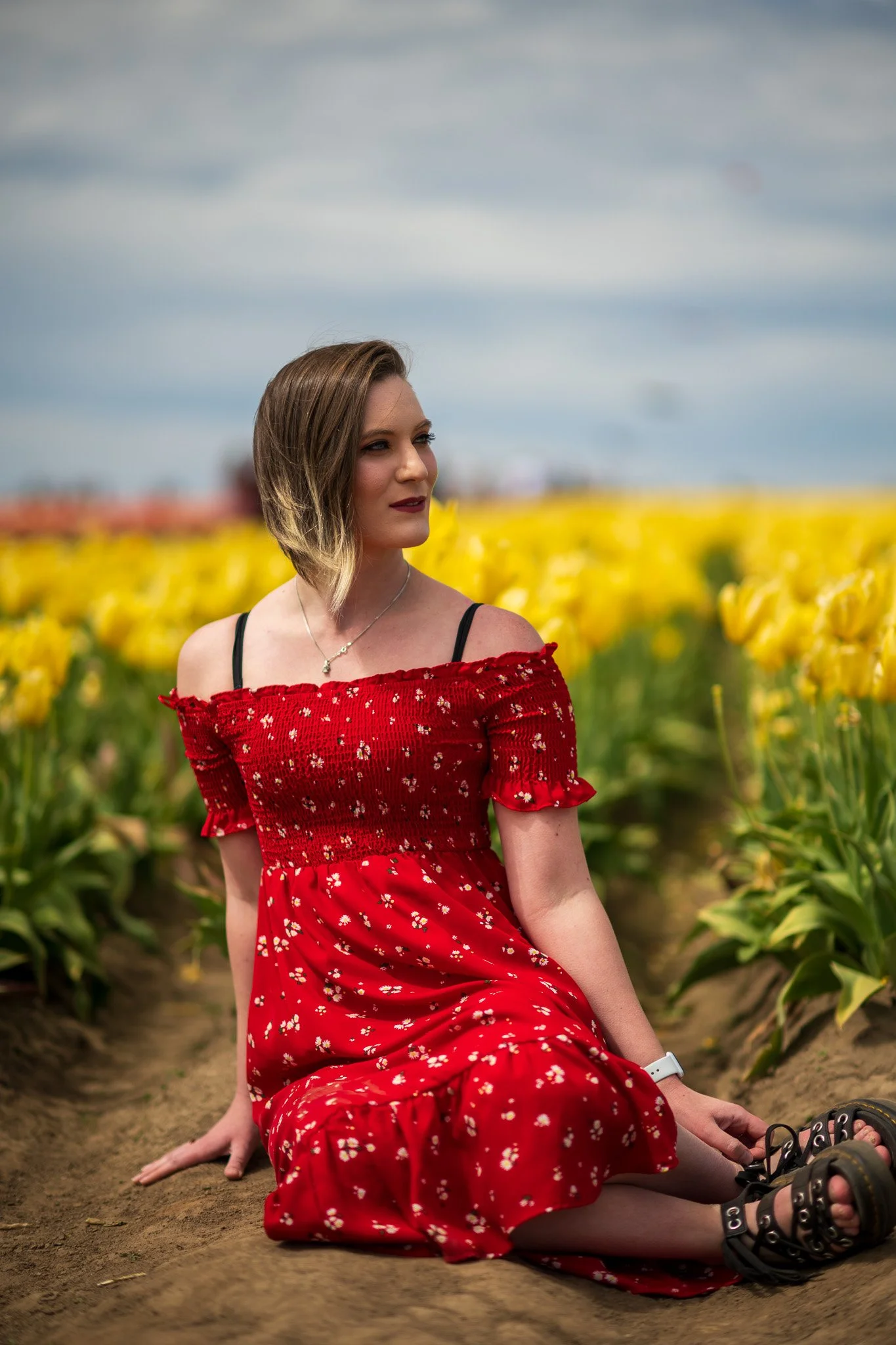 A woman sitting on the ground in a red floral dress in a tulip field.