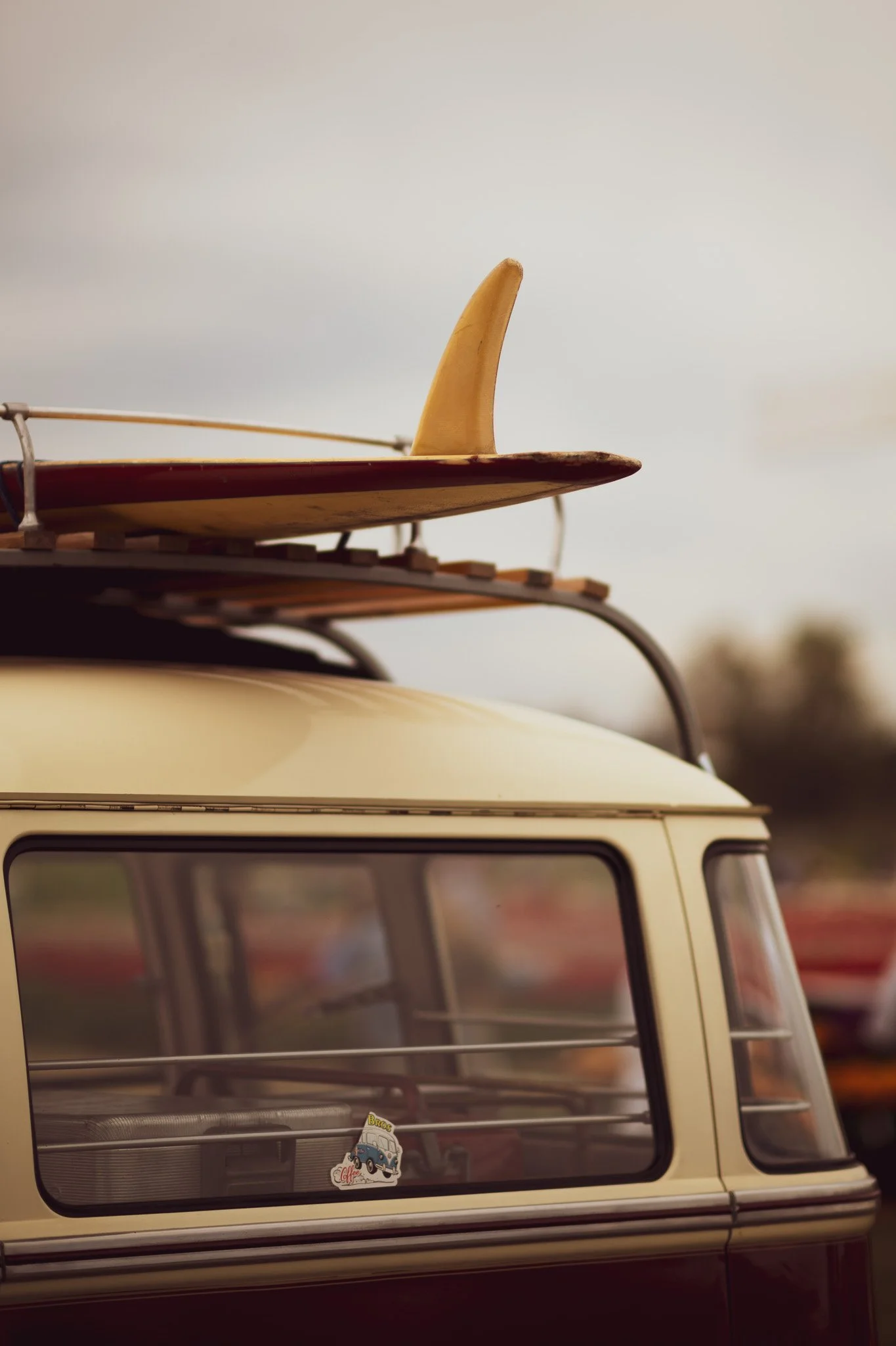 A vintage cream-colored van with a surfboard on its roof rack.