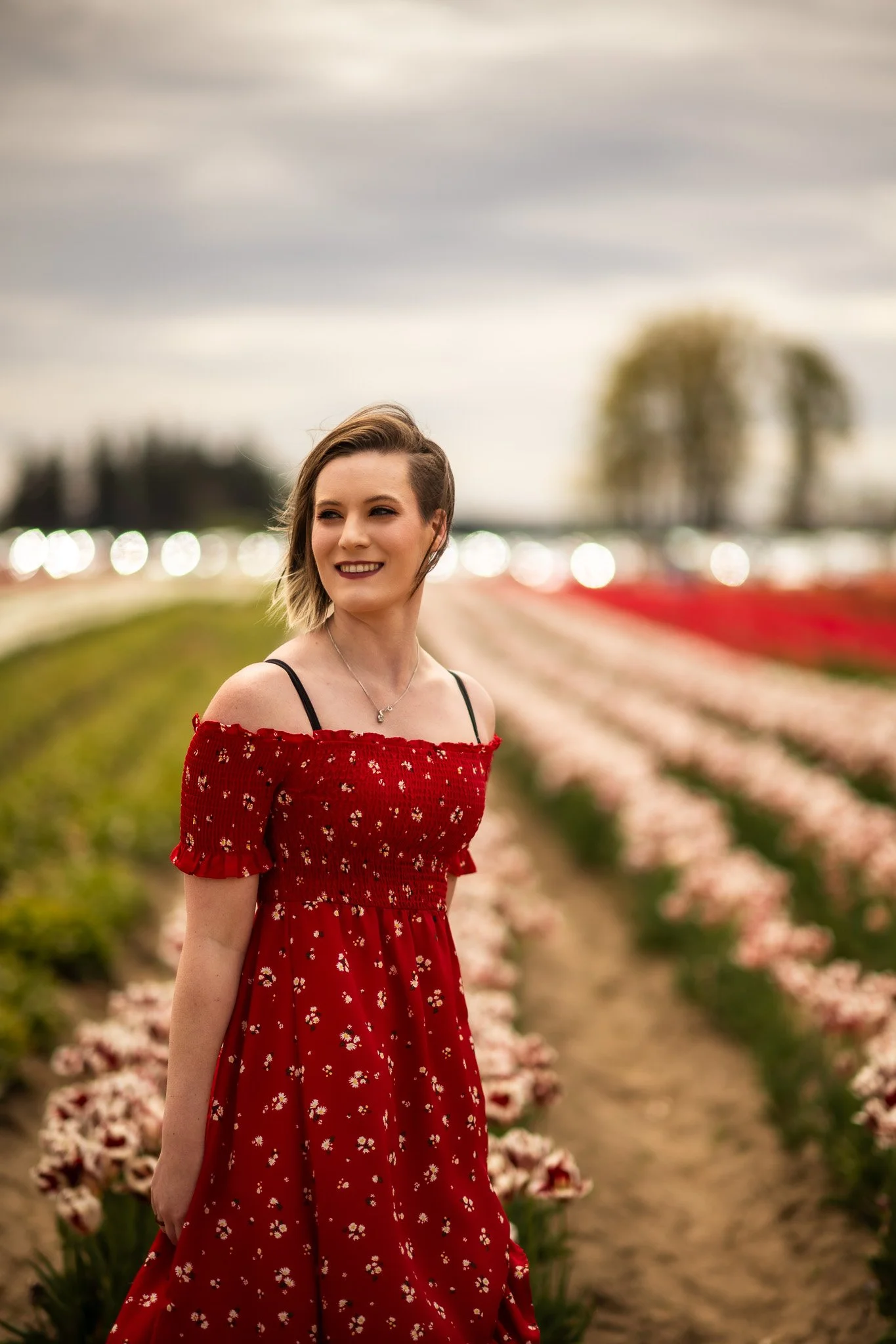 A young woman with short hair in a red floral dress standing in a flower field.