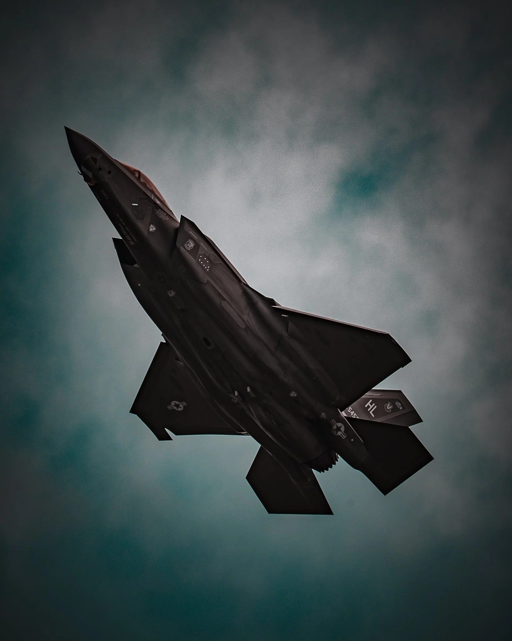 A black fighter jet flying at an angle against a cloudy sky.
