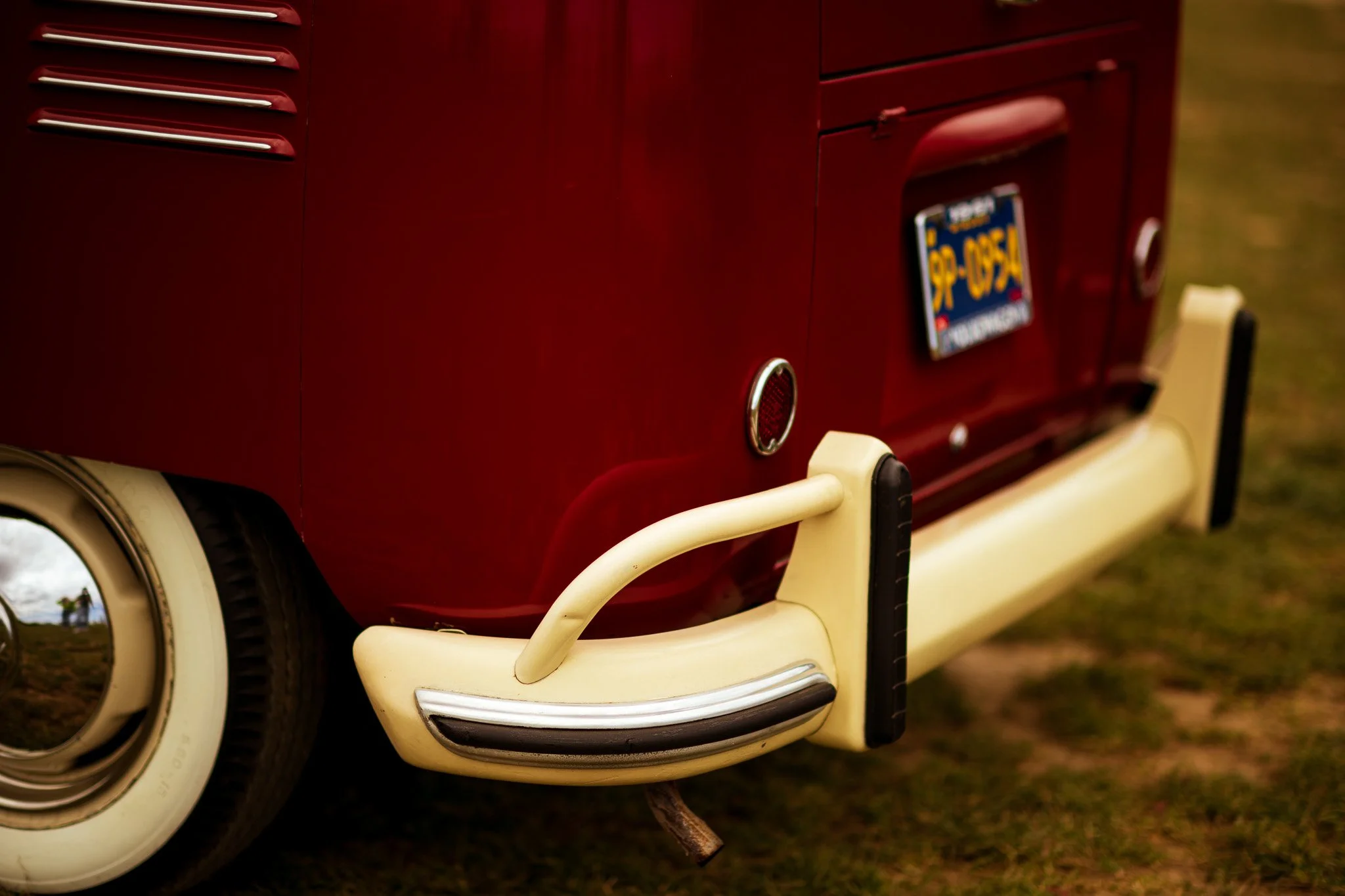 Close-up of the front bumper and license plate of a vintage red and cream-colored vehicle, possibly a van or bus, with a metal hook hanging from the bumper.