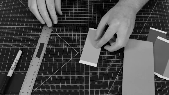 Hands working with paper models on a cutting mat, using a ruler and string for measurement.