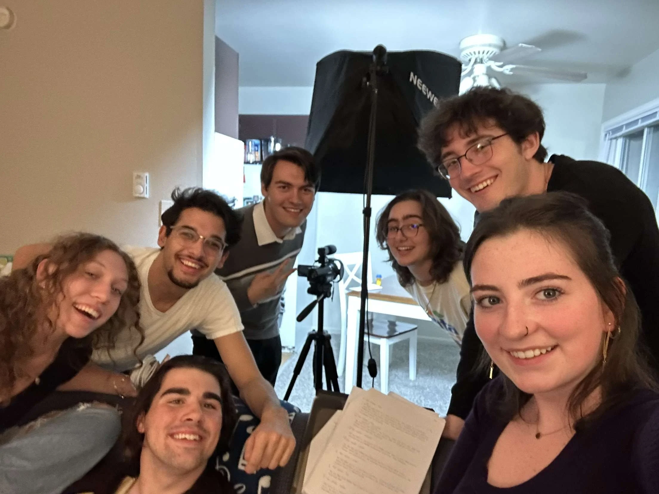 Group of seven young people smiling in a room with professional photography equipment.