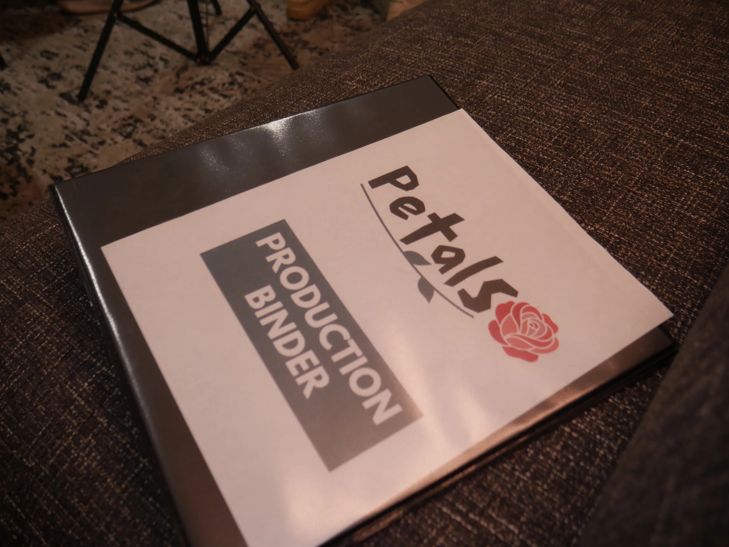 A binder with a Petalst Producation Binder label, featuring a rose graphic, placed on a brown textured fabric surface.