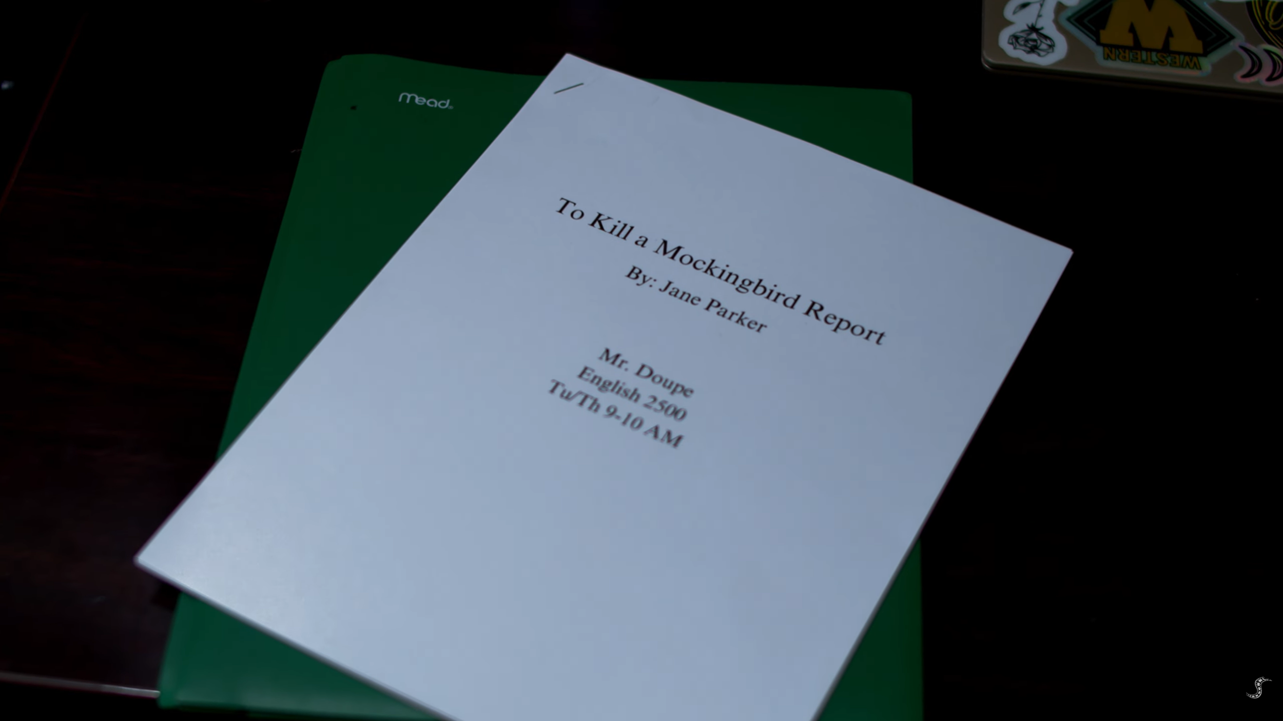 A printed report titled "To Kill a Mockingbird Report," authored by Jane Parker, for Mr. Doupe, English 2500 class, scheduled for Tuesday, 9-10 AM, is resting on a green folder on a dark wooden surface.