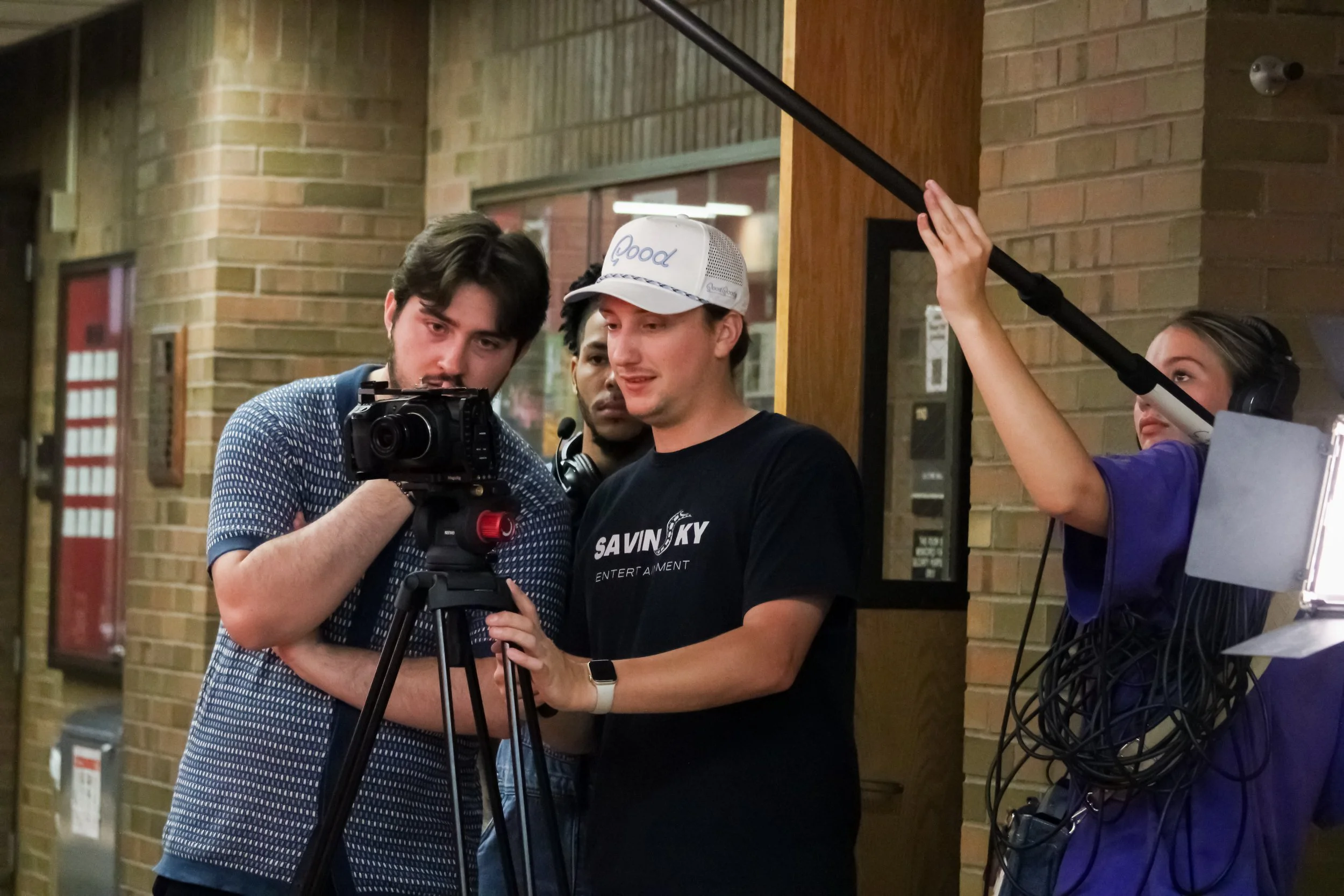 Group of people working on a film or video shoot, with one person operating a camera and another holding a boom microphone.