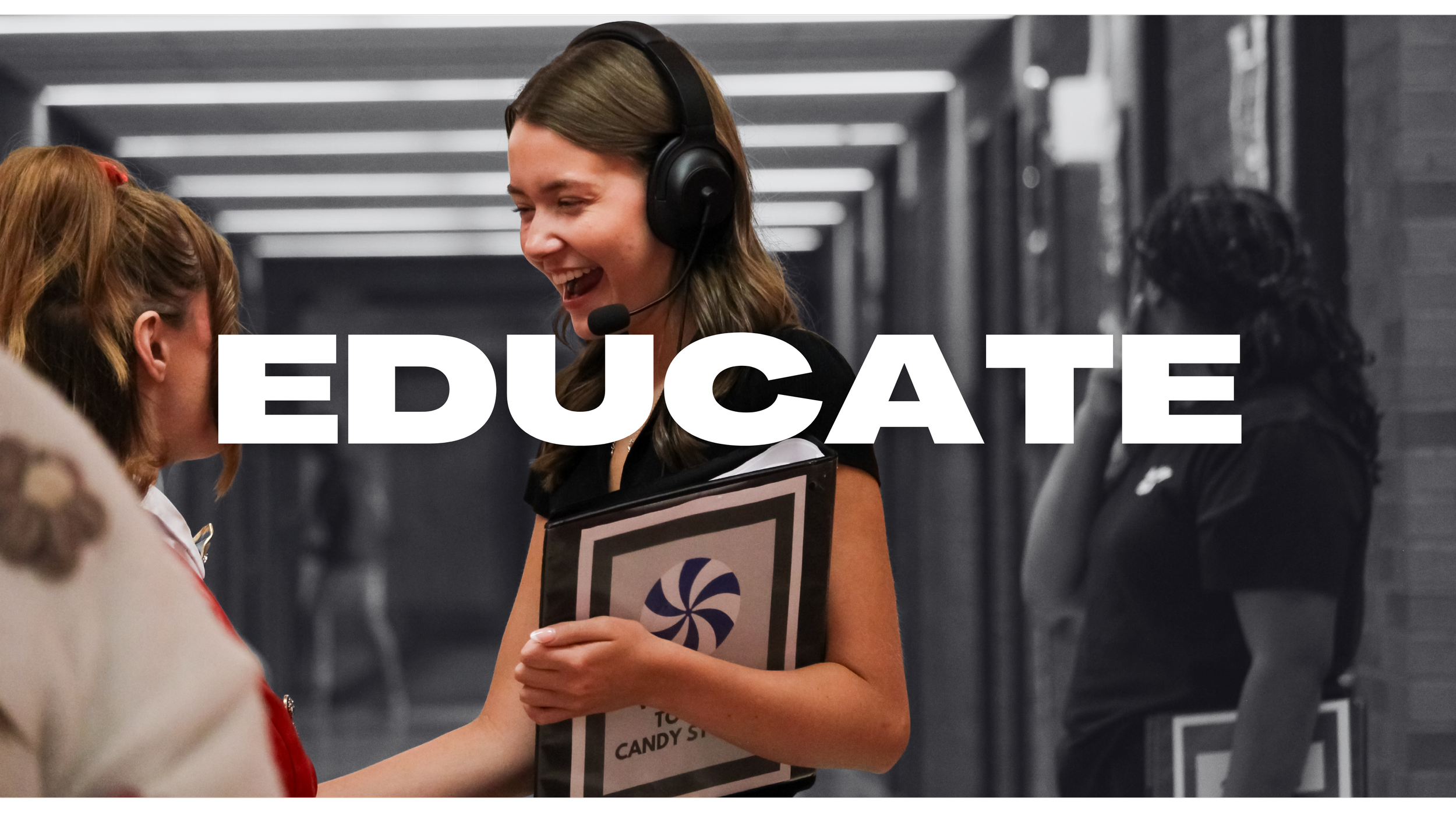 A woman wearing a headset and smiling, holding a clipboard, standing and talking to a young girl in a hallway. The word 'EDUCATE' is written across the image in large white letters.