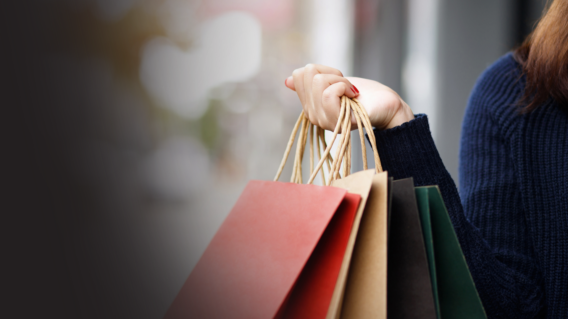 Person holding colorful shopping bags with handles in a shop window