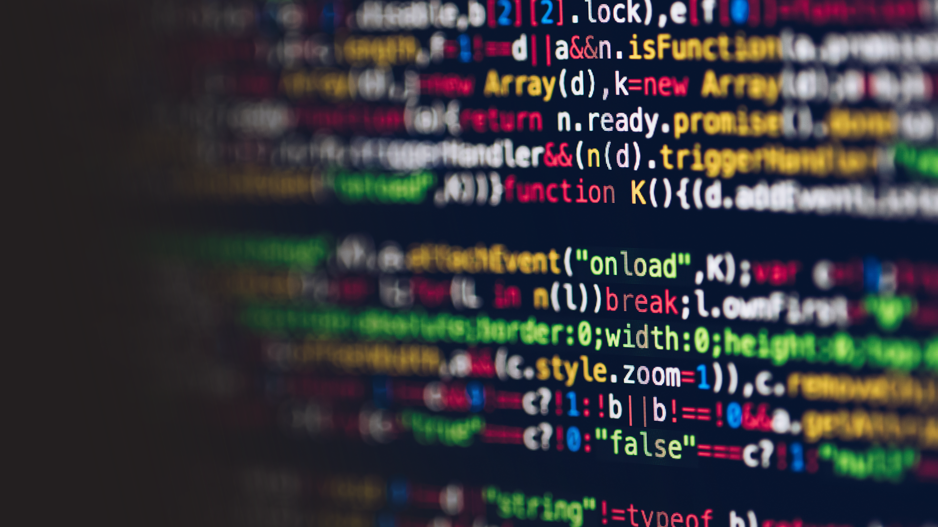 Blurred close-up of colored computer programming code on a dark screen.
