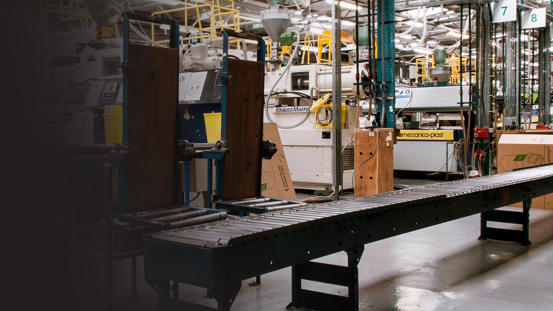 Industrial manufacturing facility with machinery, conveyor belt, and metal framework, used for packaging or processing products.