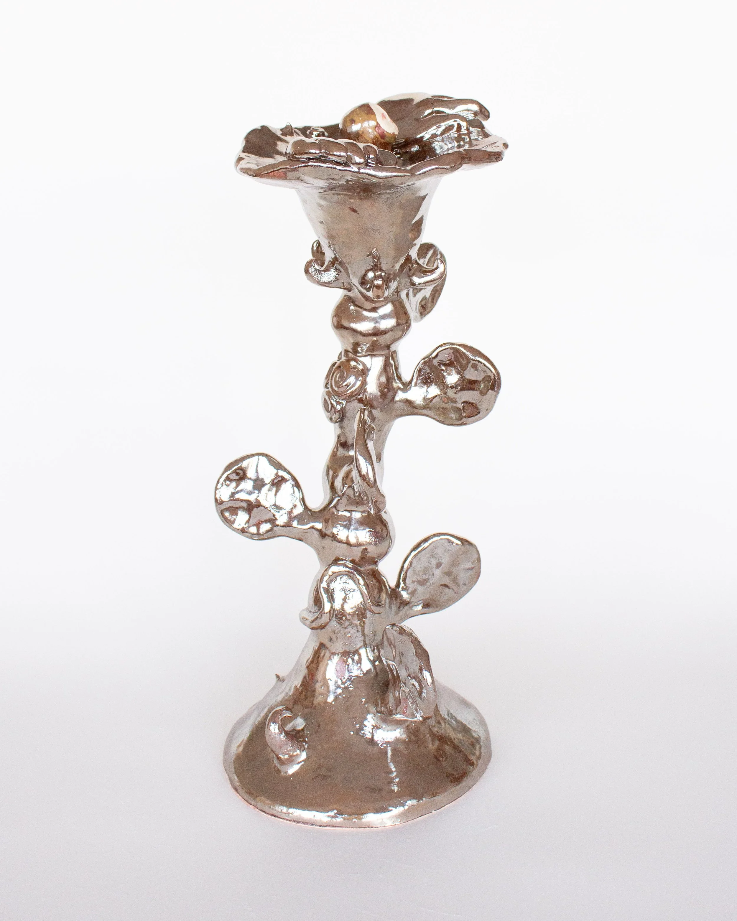 A metallic ceramic sculpture resembling a tall flower with intricate details and a small being resting inside the open top, set against a plain white background.