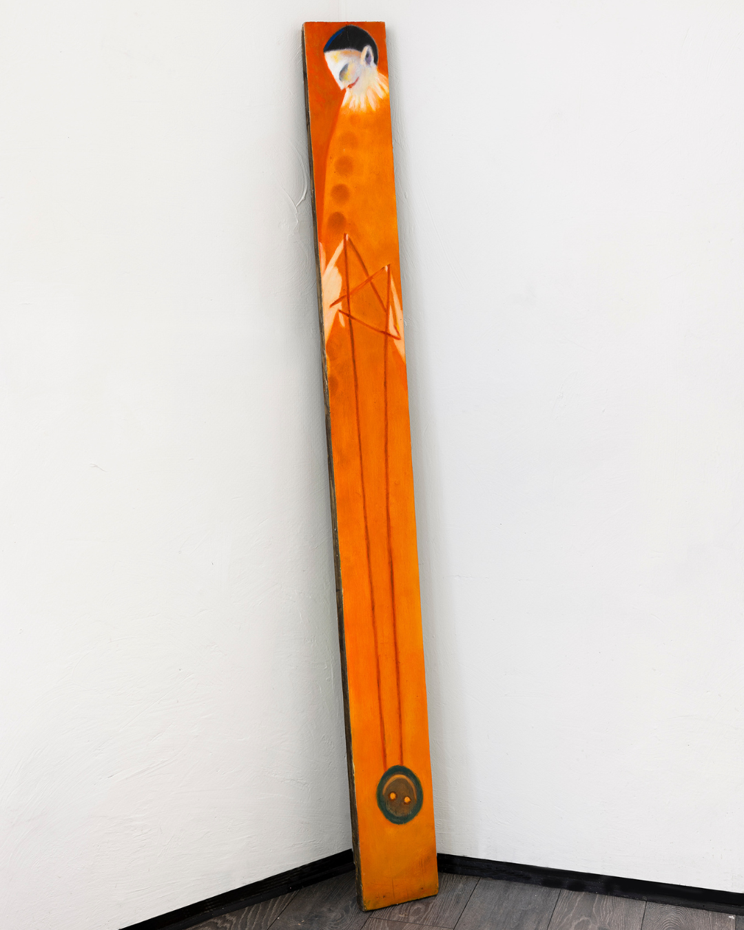 A tall, narrow wooden art piece painted with an orange background, featuring a clown playing with a yoyo.