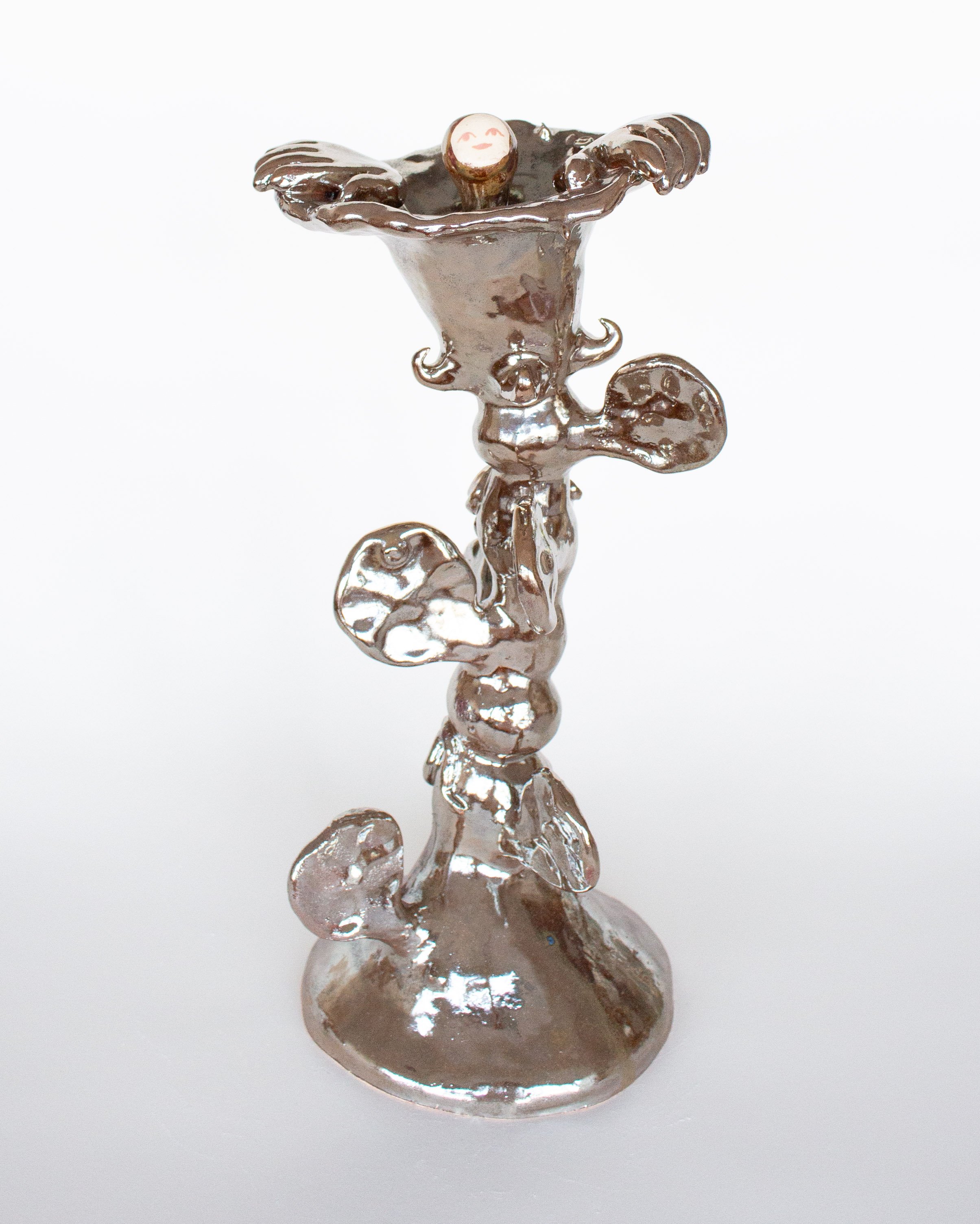 A small sculpture of a squirrel, made of shiny metal, standing on a round base, with decorative elements resembling leaves and swirls, reflecting light against a plain white background.