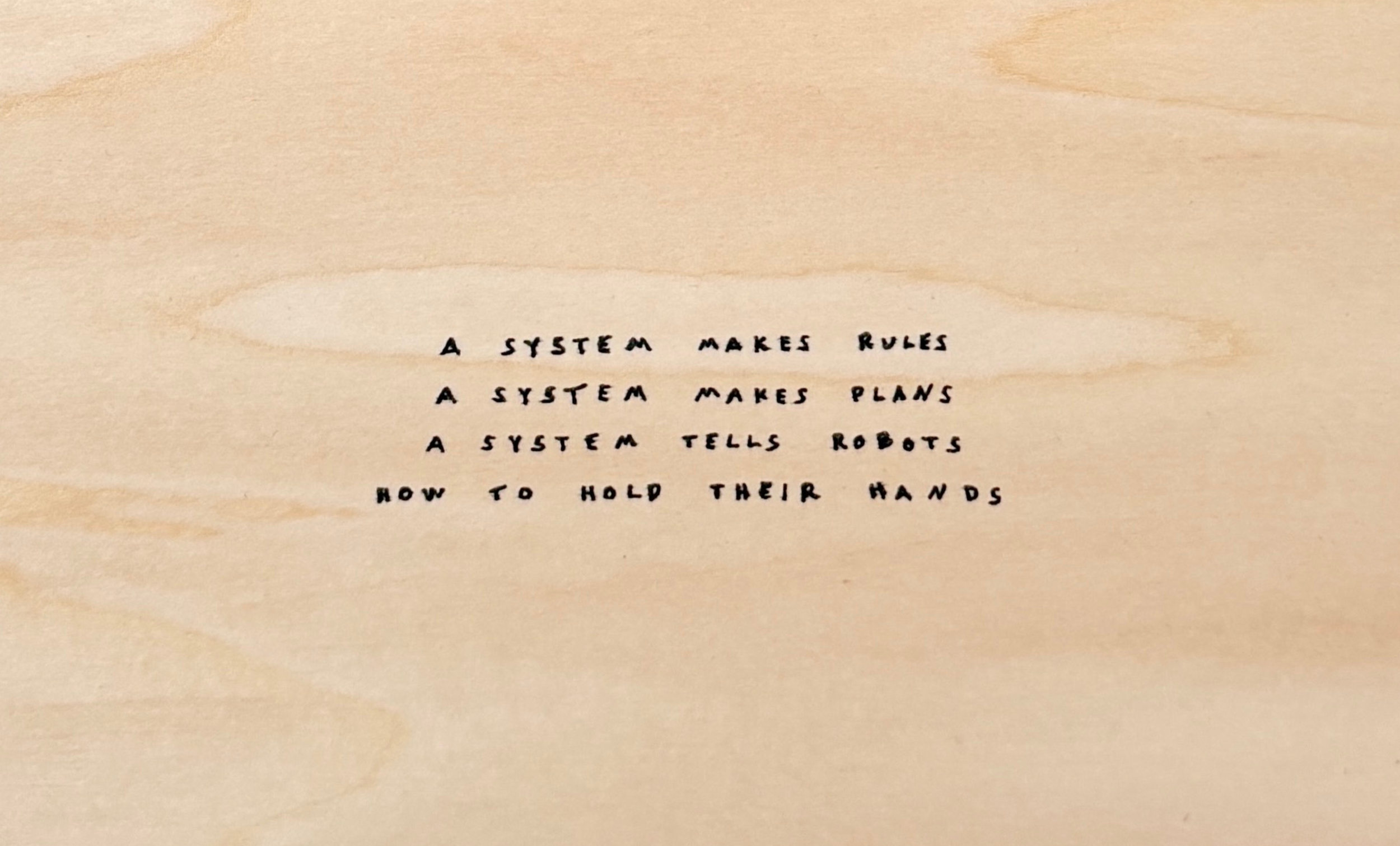 Handwritten detail on artwork that says "A SYSTEM MAKES RULES, A SYSTEM MAKES PLANS, A SYSTEM TELLS ROBOTS HOW TO HOLD THEIR HANDS."