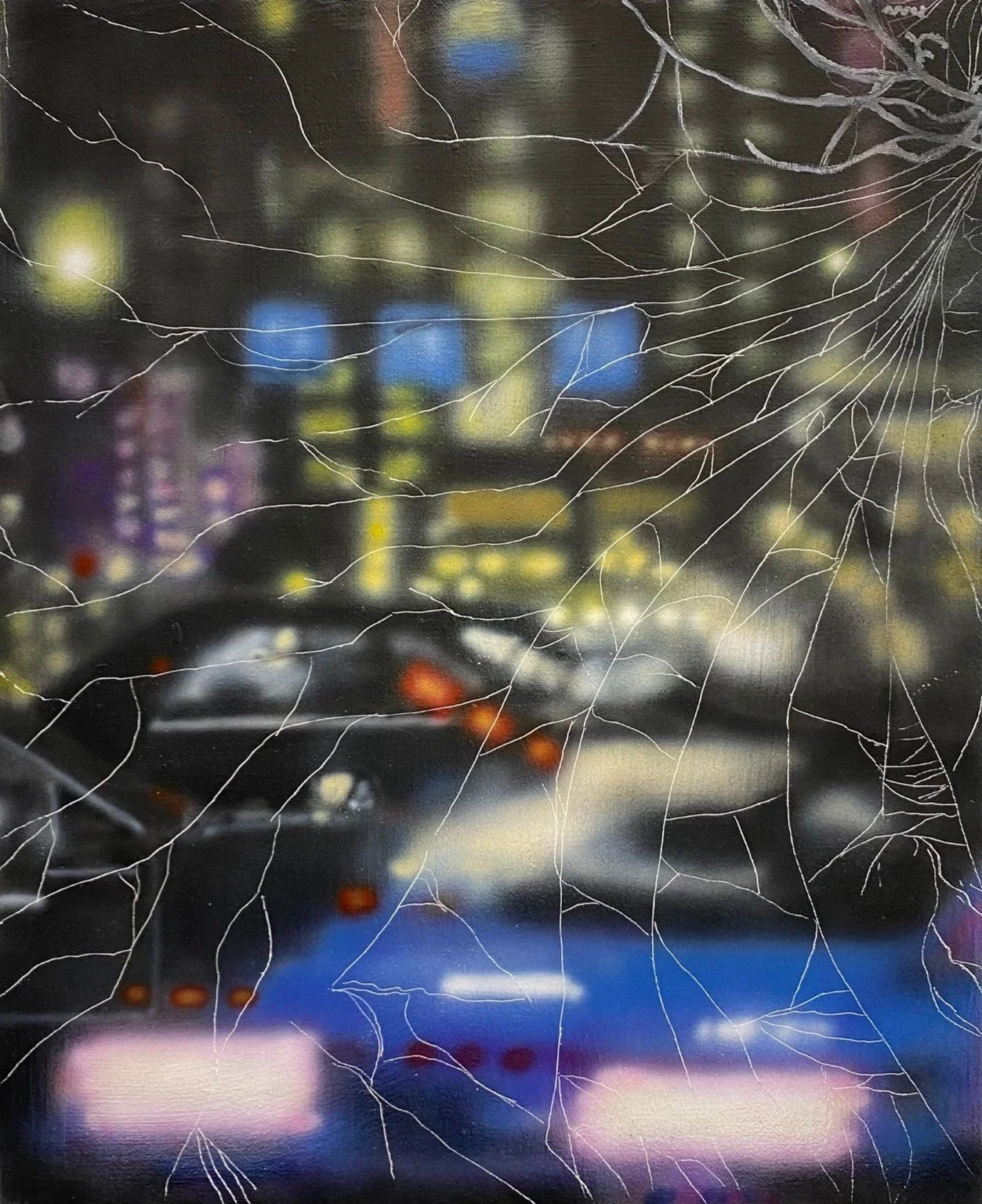 Blurred city street scene at night seen through a cracked or broken glass window with spiderweb-like cracks.