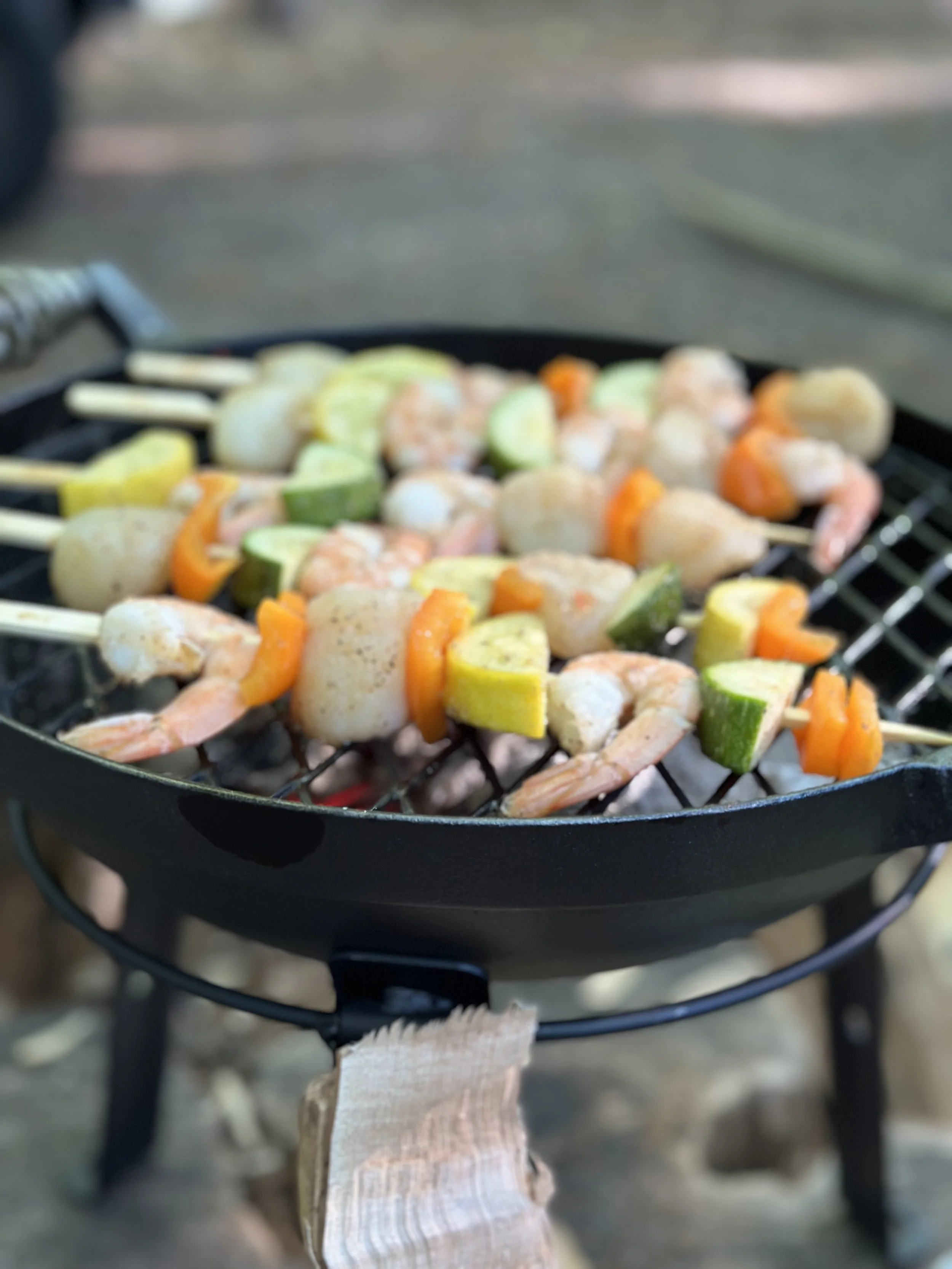 Shrimp and vegetable skewers grilling on a barbecue with zucchini, yellow squash, and orange bell peppers.