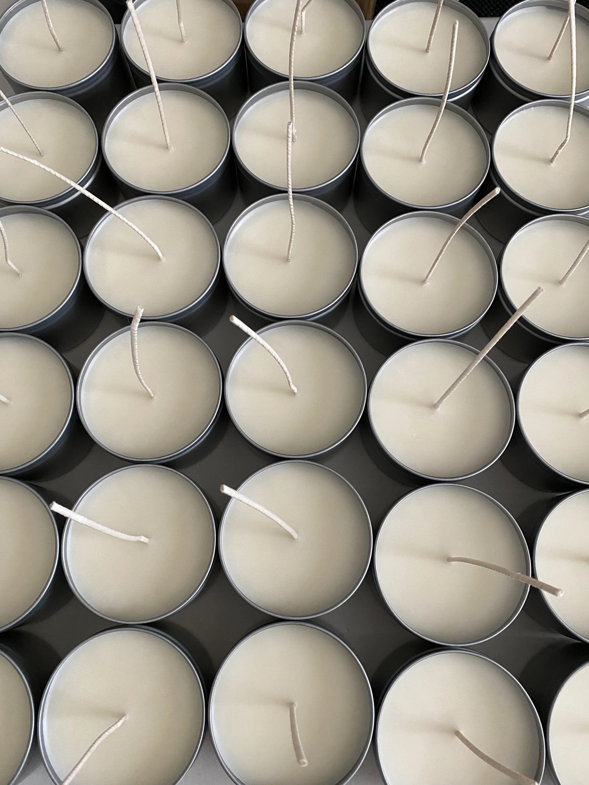 A collection of white candles in silver tins with unlit wicks.