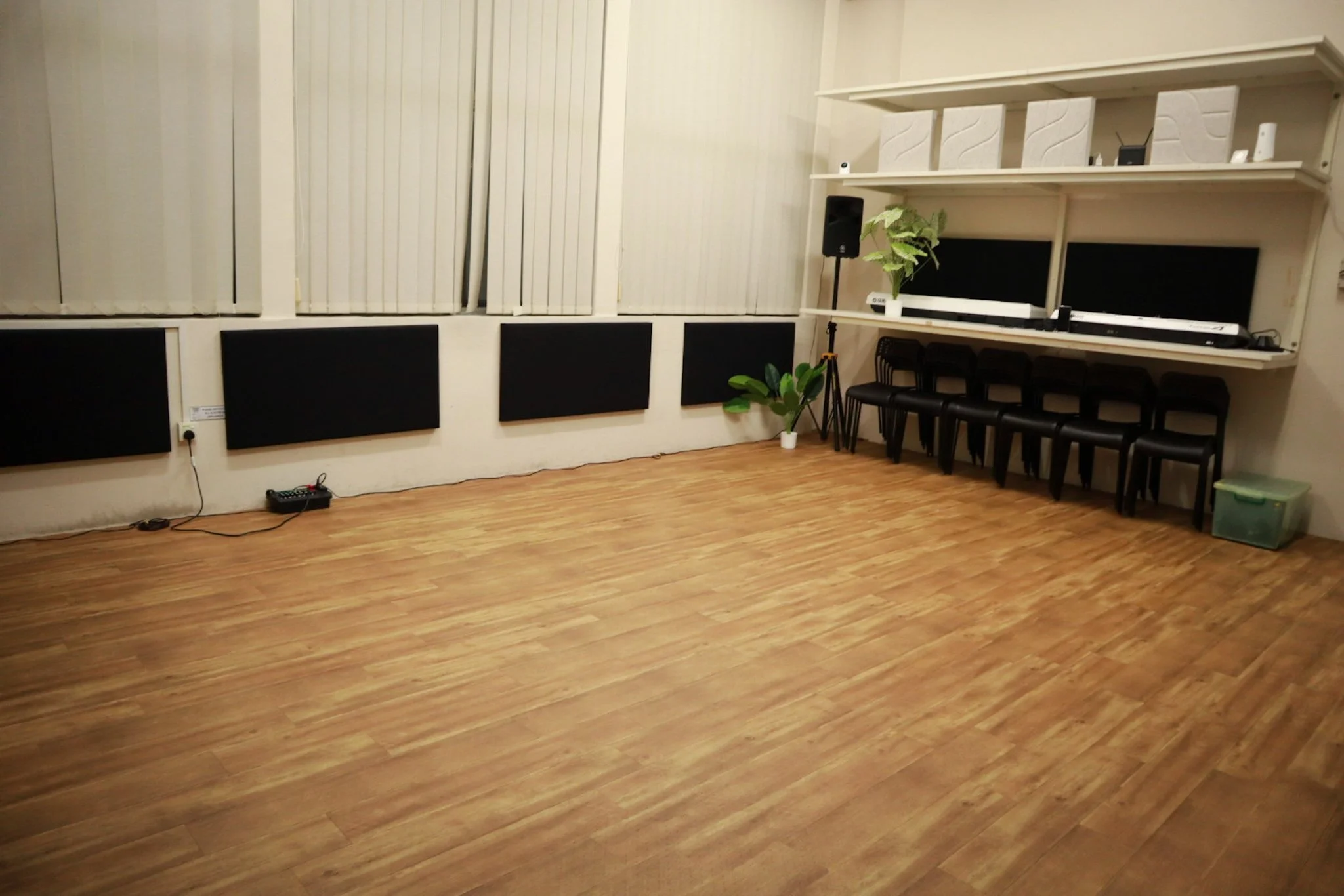 Empty room with large windows and vertical blinds, four black wall-mounted panels, hardwood floor.