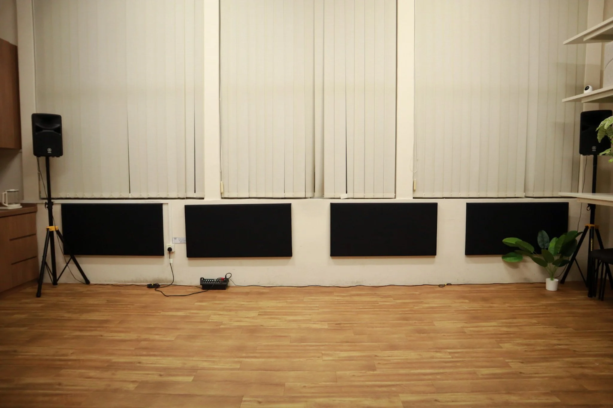 Empty room with large windows and vertical blinds, four black wall-mounted panels, hardwood floor.