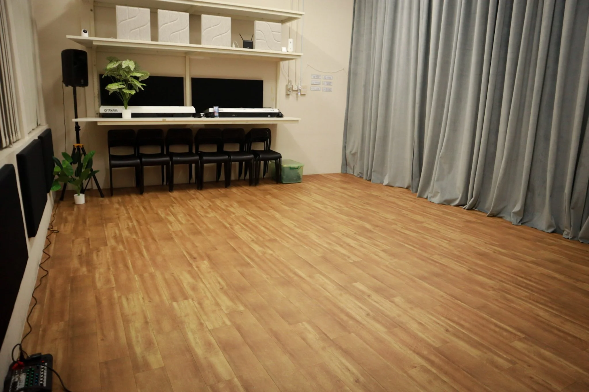 Empty room with large windows and vertical blinds, four black wall-mounted panels, hardwood floor.