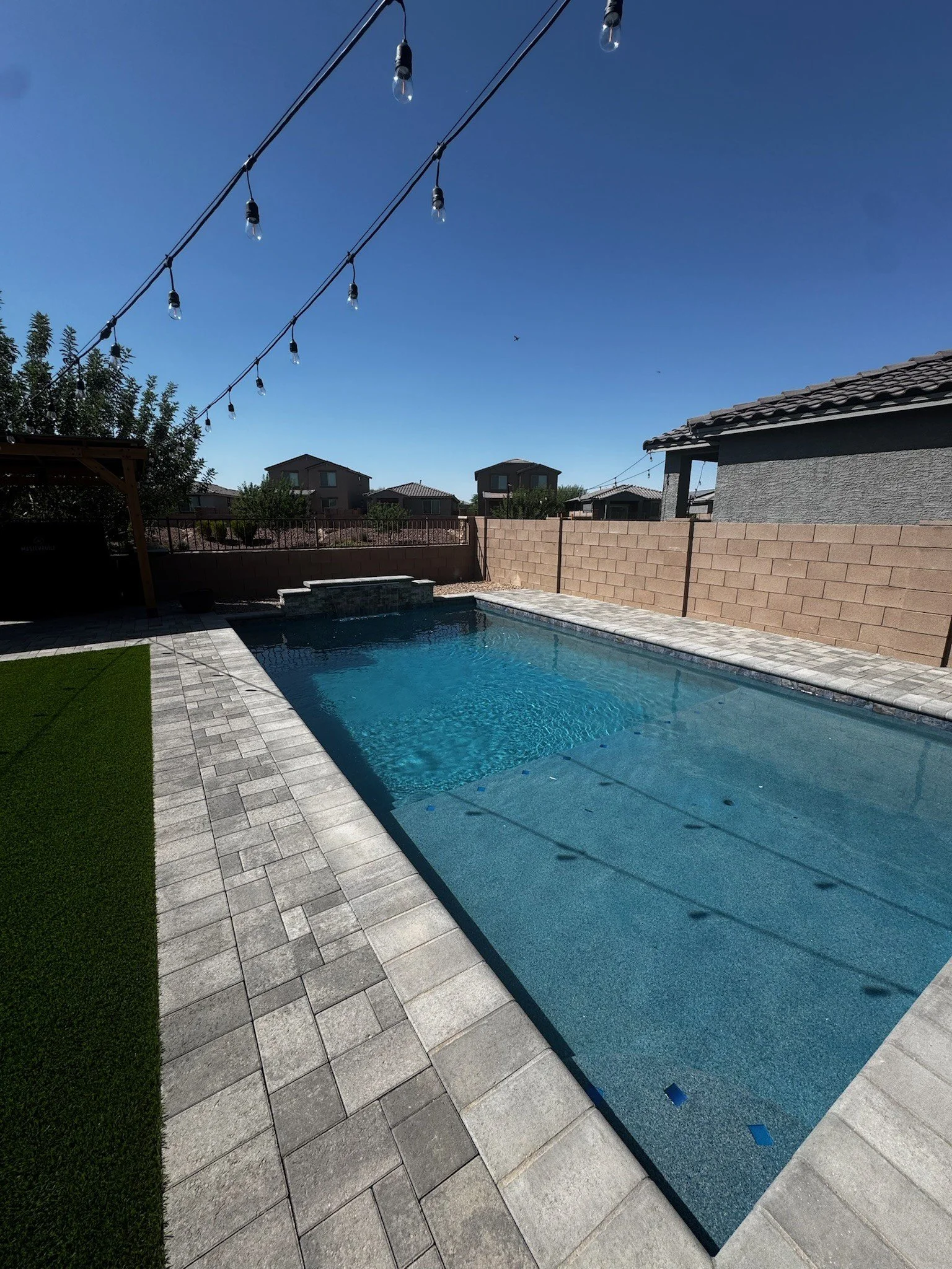 Geometric custom pool with festoon string lights and turf landscaping by Meraki Pools AZ in Tucson, Arizona.