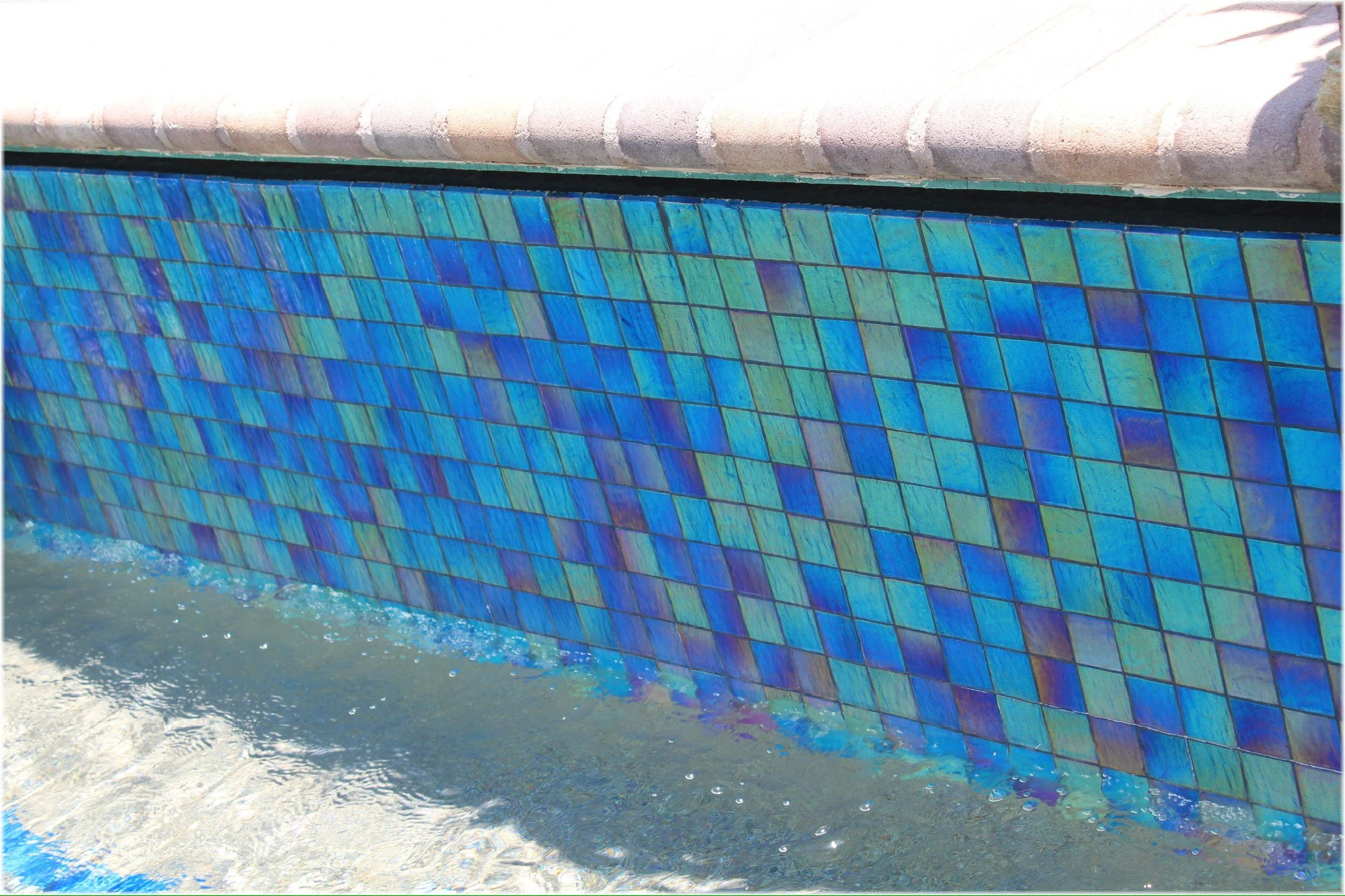 Close-up of vibrant blue glass pool tile and travertine paver decking, custom finish by Meraki Pools AZ in Tucson, Arizona.