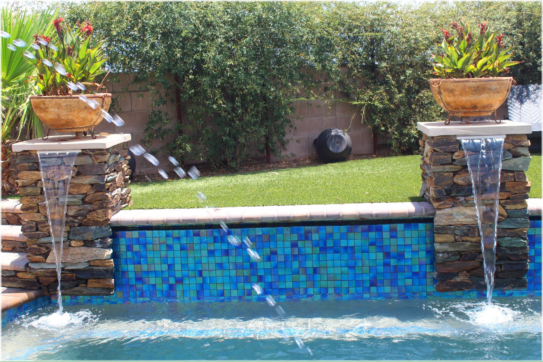 Custom freeform pool with a Baja shelf, blue glass tile, and stacked-stone water features by Meraki Pools AZ, Tucson, Arizona.