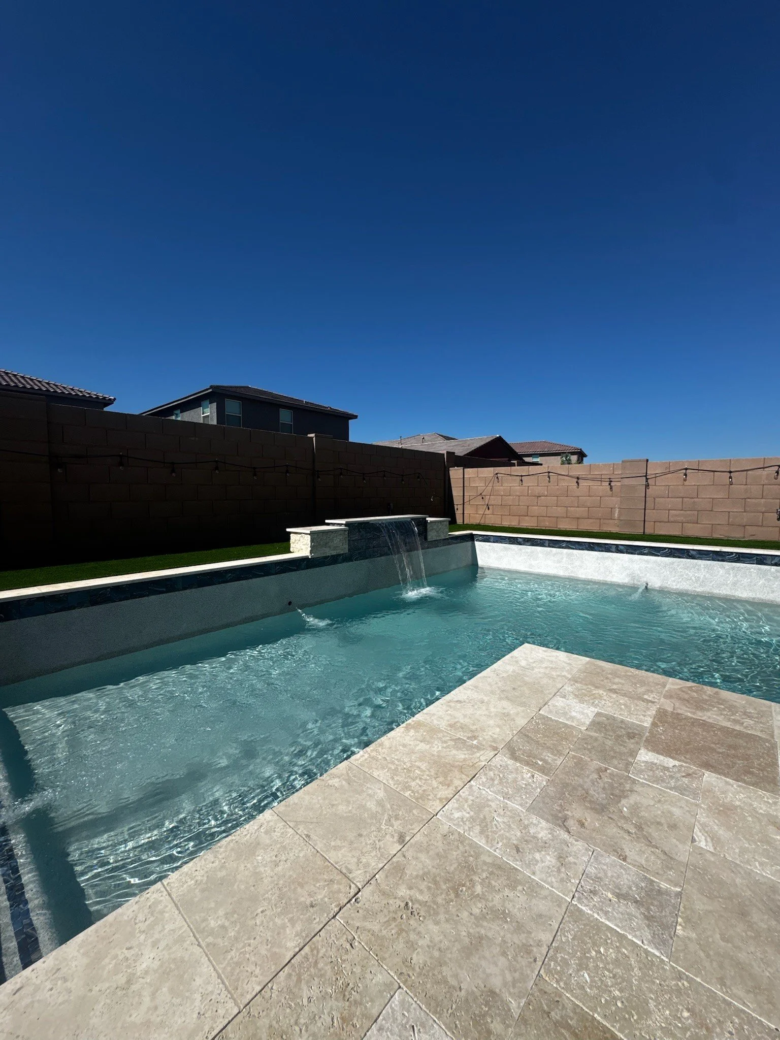 Custom rectangular pool with travertine decking and outdoor seating by Meraki Pools AZ in Tucson, Arizona.