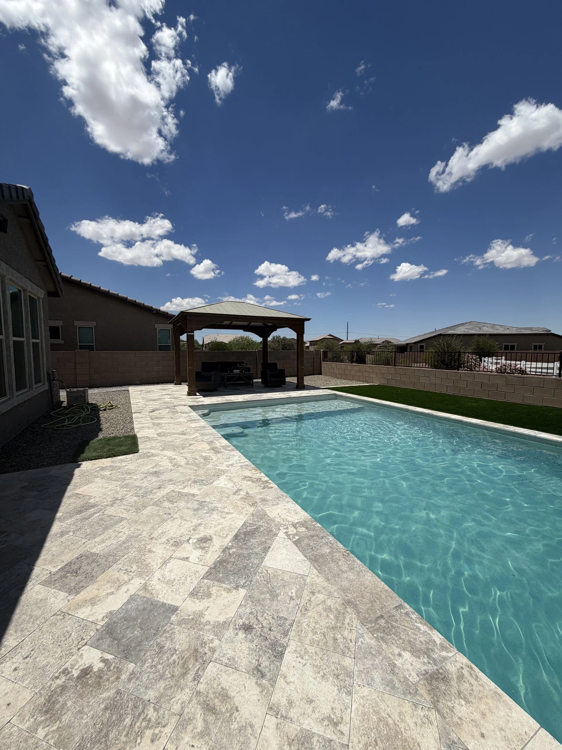 Custom pool at dusk with a shaded ramada and travertine deck, by Meraki Pools AZ in Tucson, Arizona.
