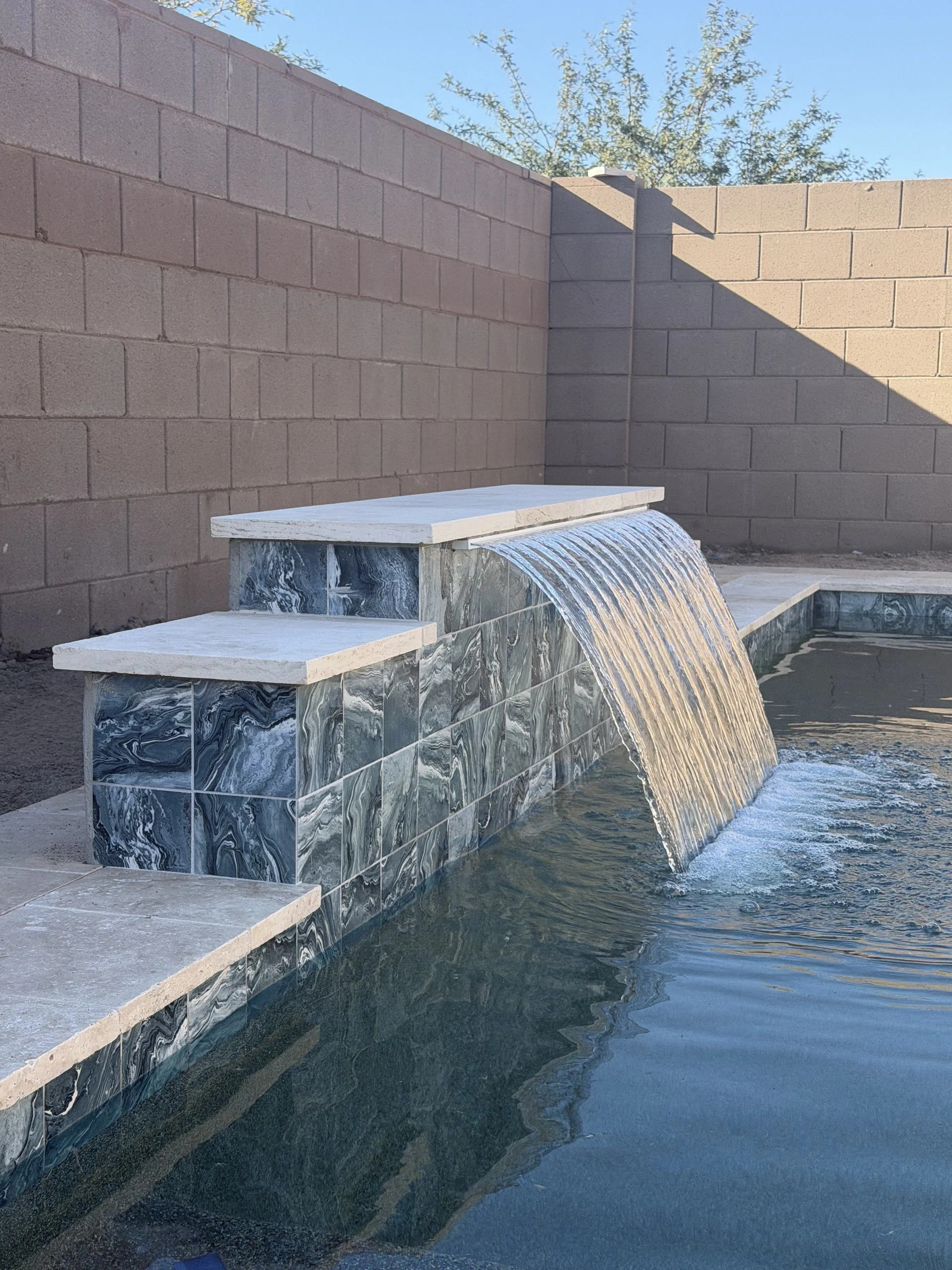 Custom pool water feature with a sheer-descent waterfall over a stacked-stone wall, built by Meraki Pools AZ in Tucson, Arizona.
