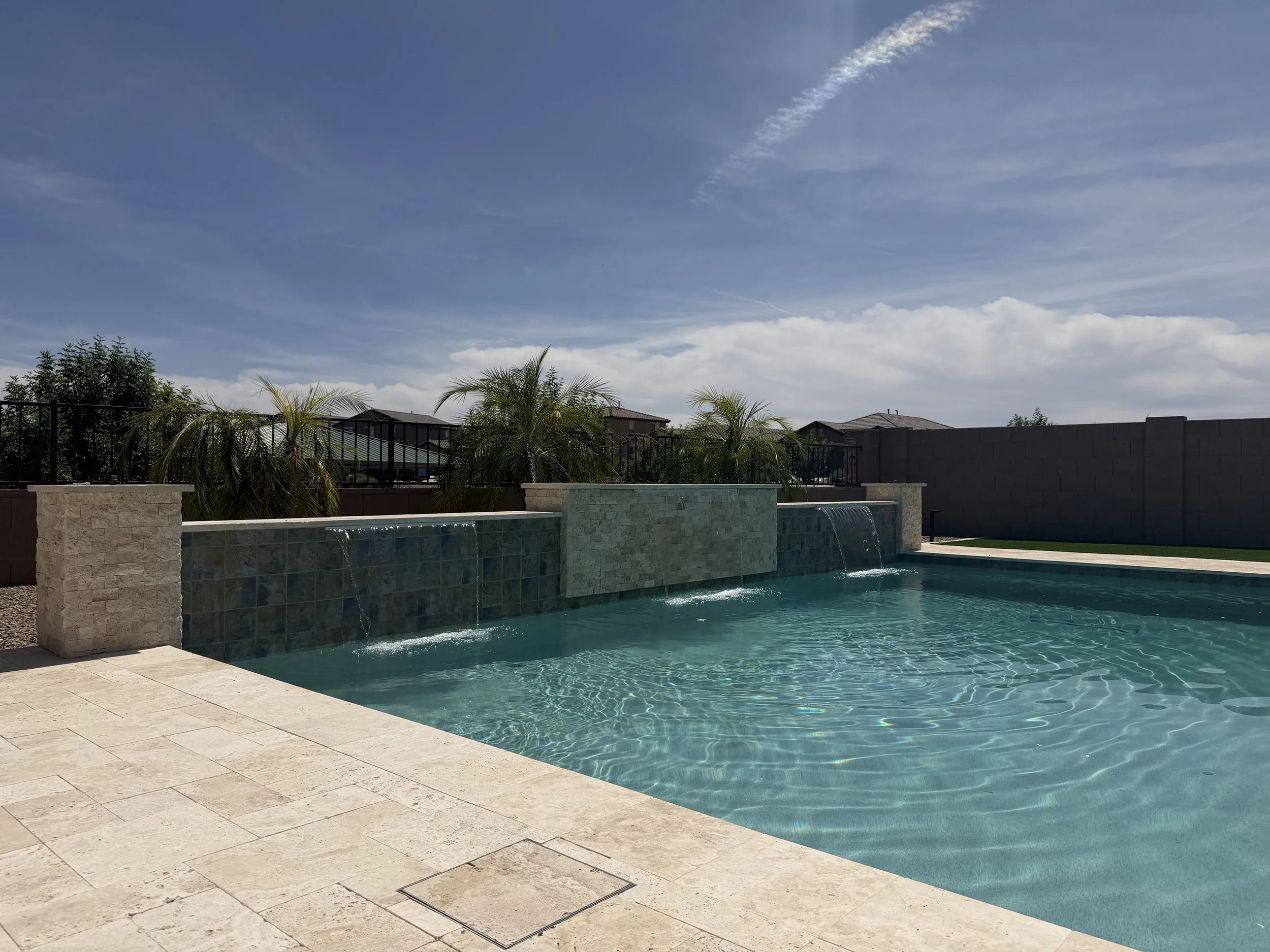 Custom modern pool with a sheer-descent water feature and travertine deck, built by Meraki Pools AZ in Tucson, Arizona.