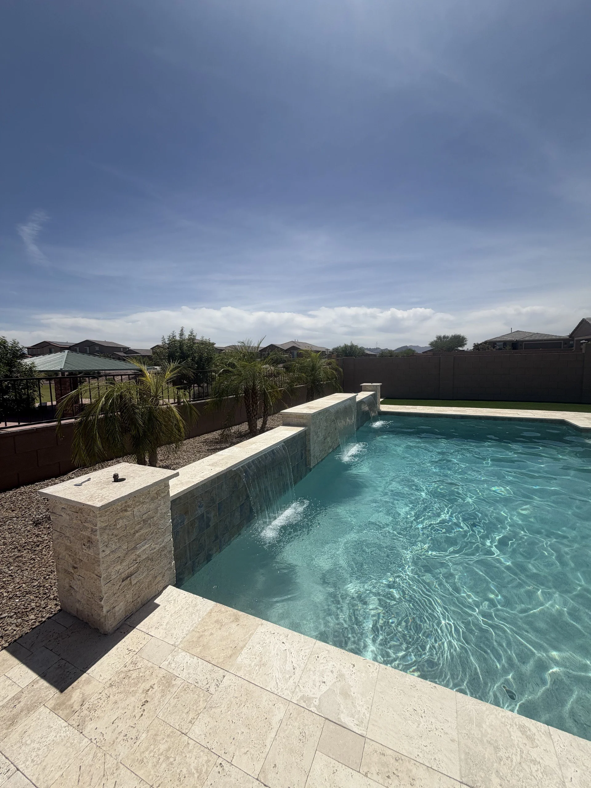 Modern custom swimming pool with a sheer-descent water feature, raised wall, and travertine pool deck, designed and built by Meraki Pools AZ in Tucson, Arizona.