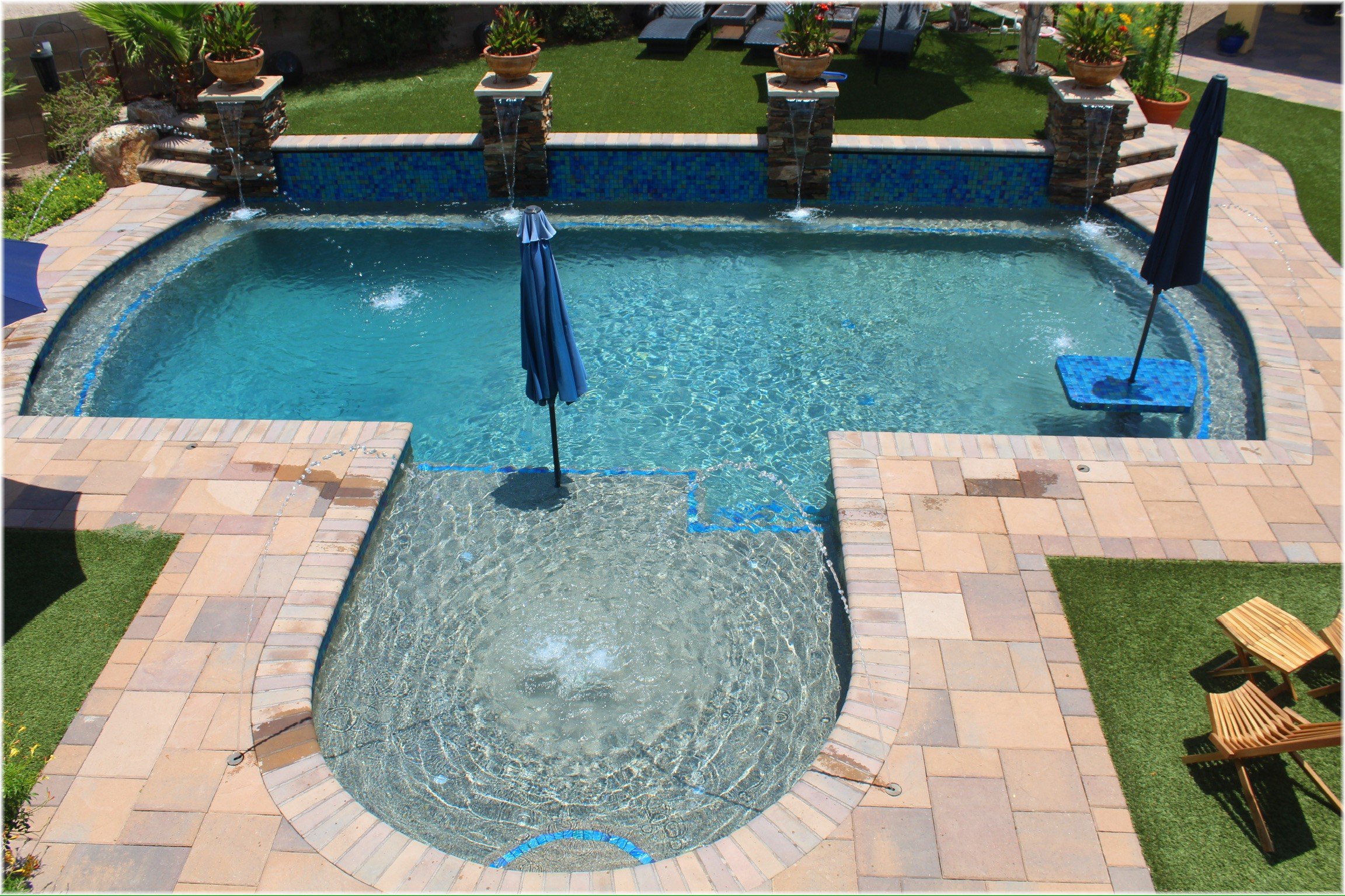 Freeform resort-style swimming pool with deck-jet water features and travertine decking, custom-built by Meraki Pools AZ in Tucson, Arizona.