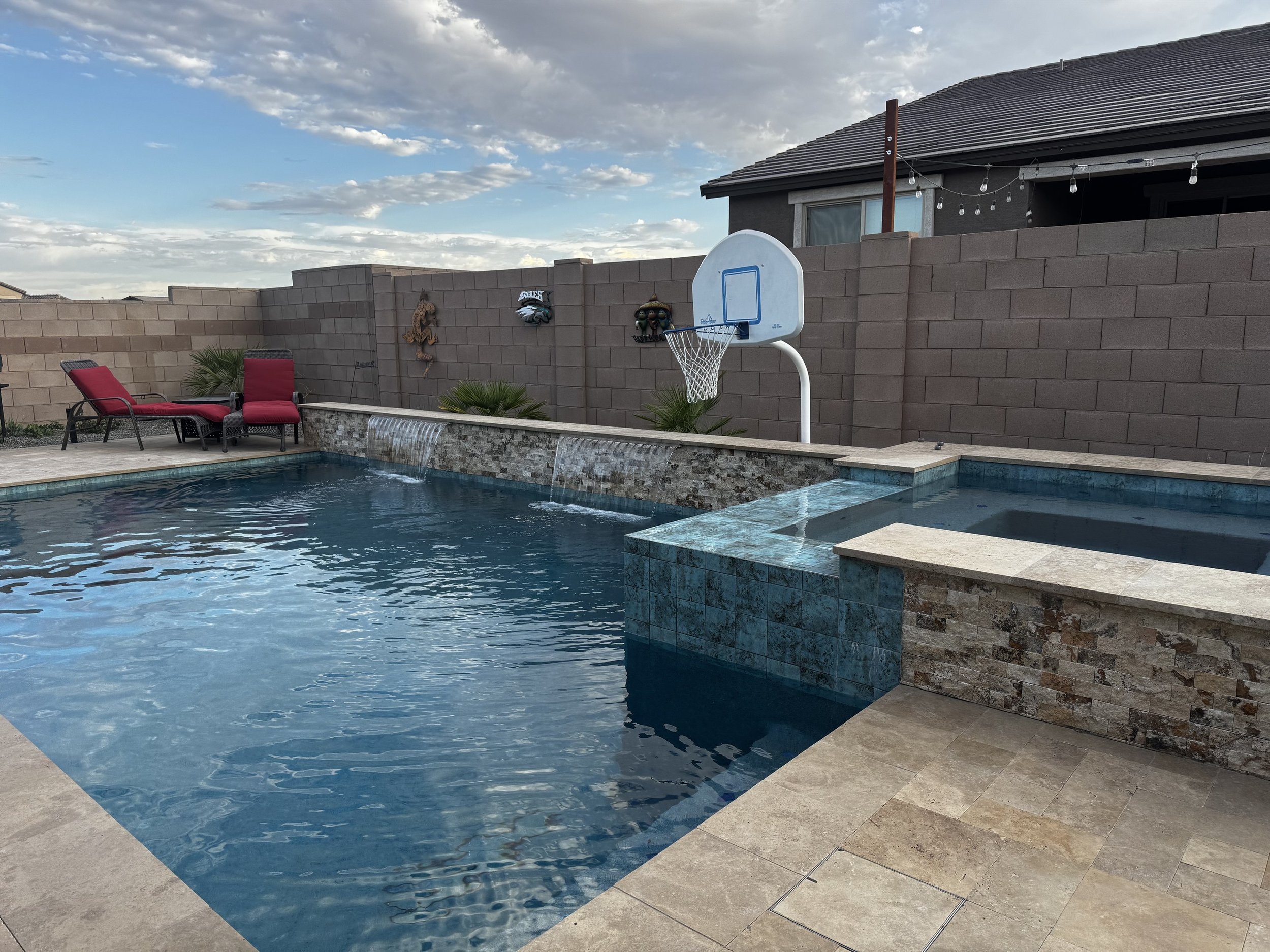 Custom backyard pool with a raised spa and spillways, surrounded by paver decking, by Meraki Pools AZ in Tucson, Arizona.