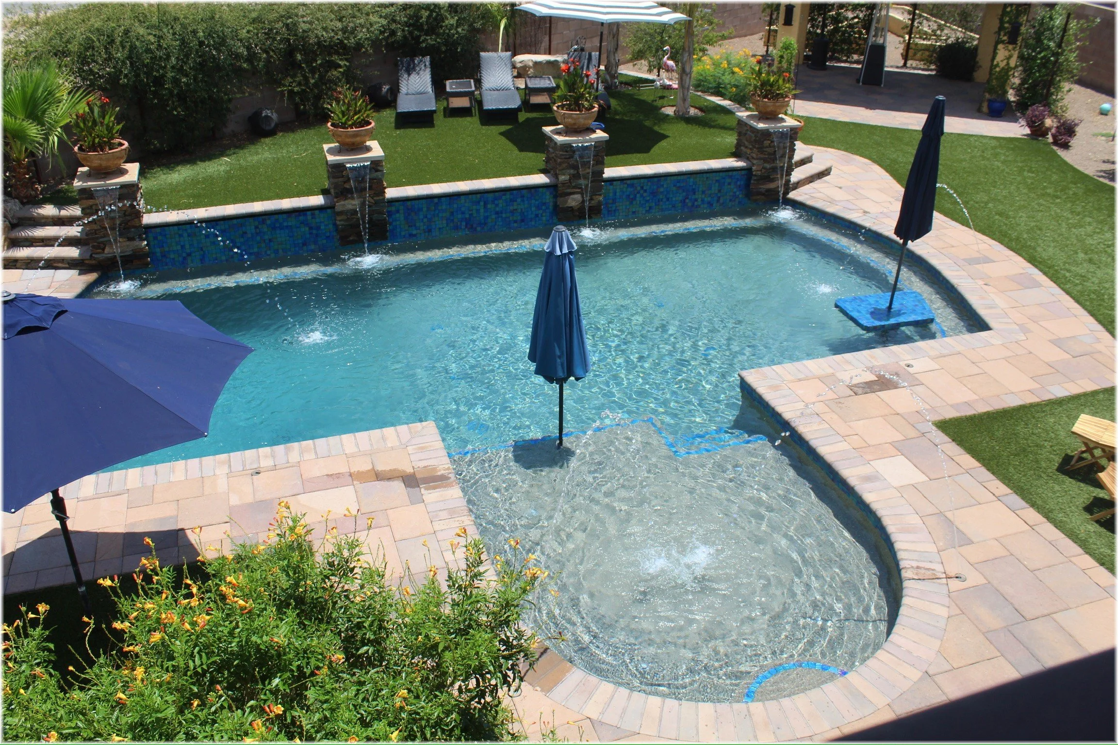 Freeform custom pool with blue glass tile, scupper water features, and paver decking, a backyard oasis by Meraki Pools AZ in Tucson, Arizona.