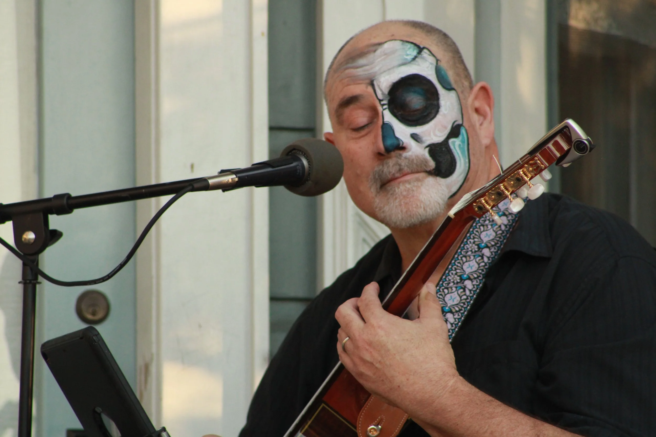 A man with face paint resembling a skull, playing guitar with closed eyes in front of a microphone. Weddings. Corporate Events. Private Parties. City Festivals. Tribute Shows. Live Band Burlesque. Tributonic.