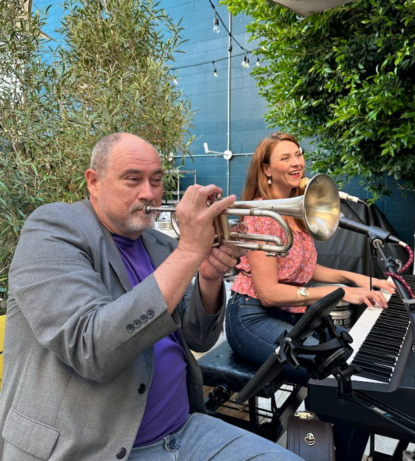 A man playing trumpet and a woman playing piano outdoors, with greenery and string lights in the background. Weddings. Corporate Events. Private Parties. City Festivals. Tribute Shows. Live Band Burlesque. Tributonic.